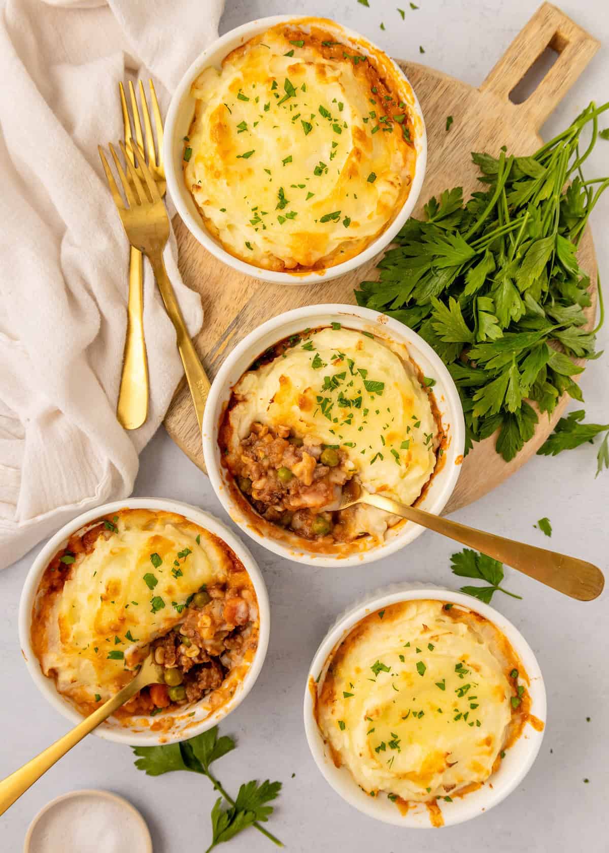 Four Mini Shepard Pies topped with mashed potatoes and herbs, served with golden forks.