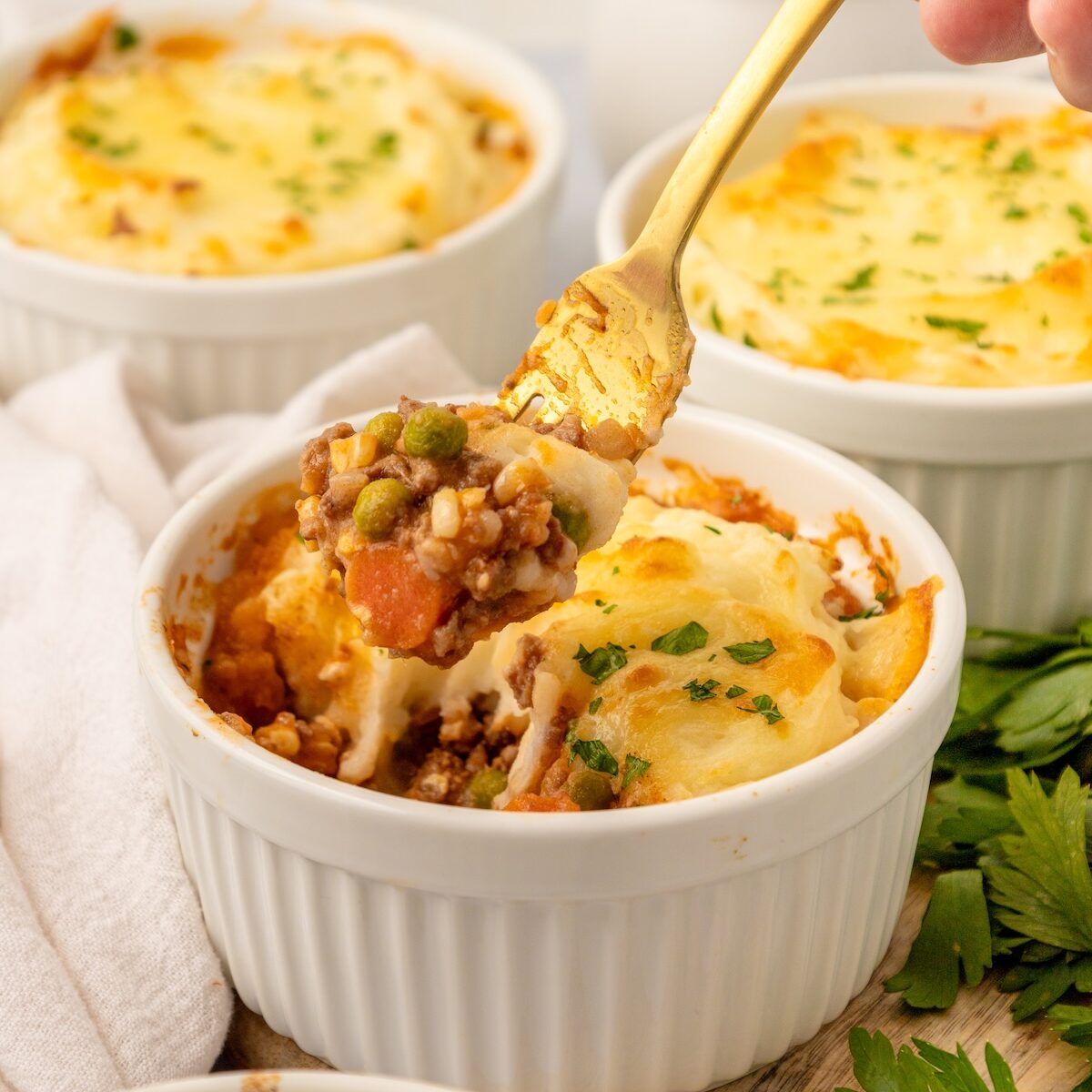 A fork scoops Mini Shepherd Pies from a white ramekin, topped with melted cheese and parsley.