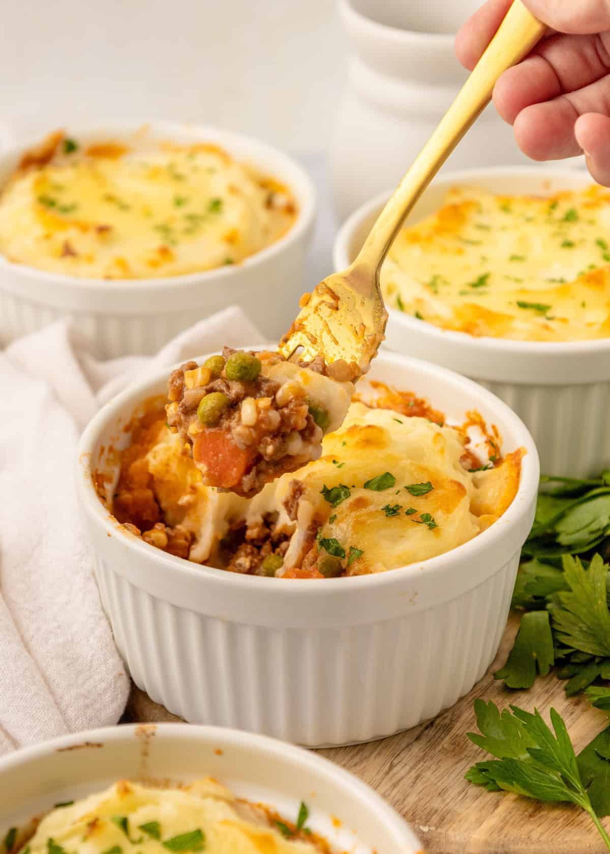 A fork scoops Mini Shepherd Pies from a white ramekin, topped with melted cheese and parsley.