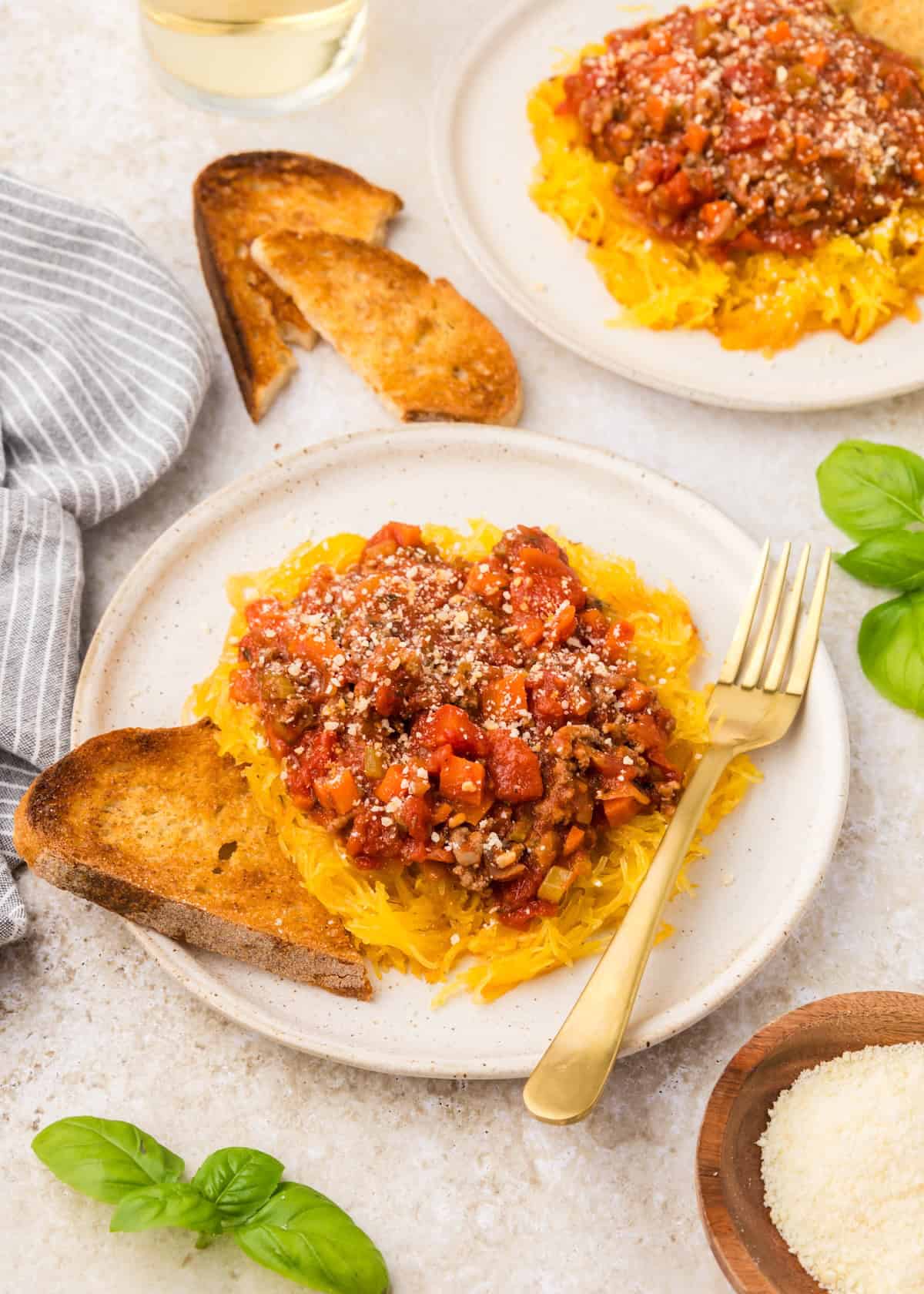 Plate of spaghetti squash bolognese with toast and a gold fork on a white surface.