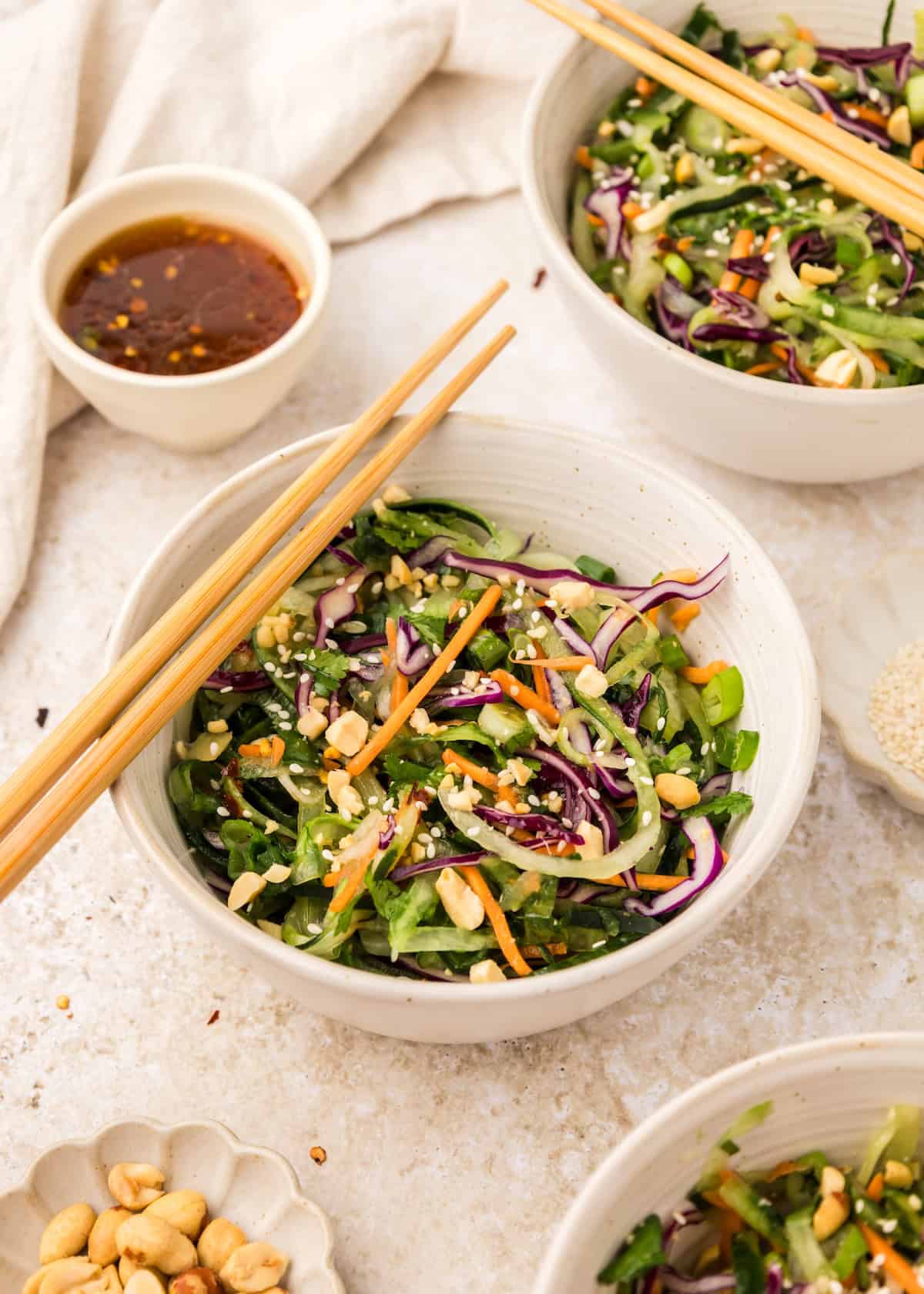 Bowl of Asian Cucumber Noodle Salad with chopsticks, peanuts, and dipping sauce on the side.