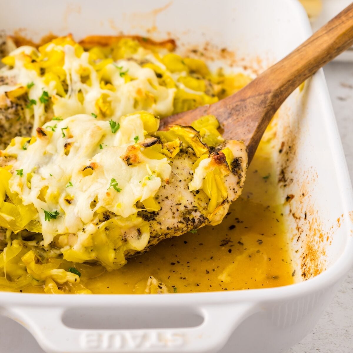 A wooden spoon serves Banana Pepper Chicken topped with cheese from a white dish.