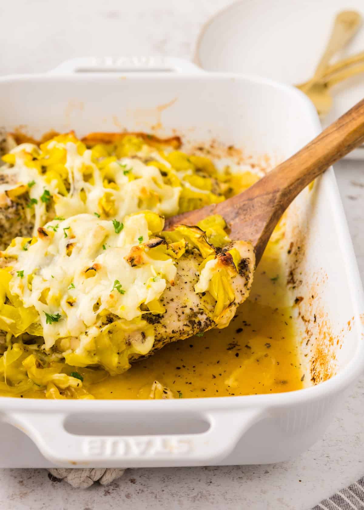 A wooden spoon serves Banana Pepper Chicken topped with cheese from a white dish.