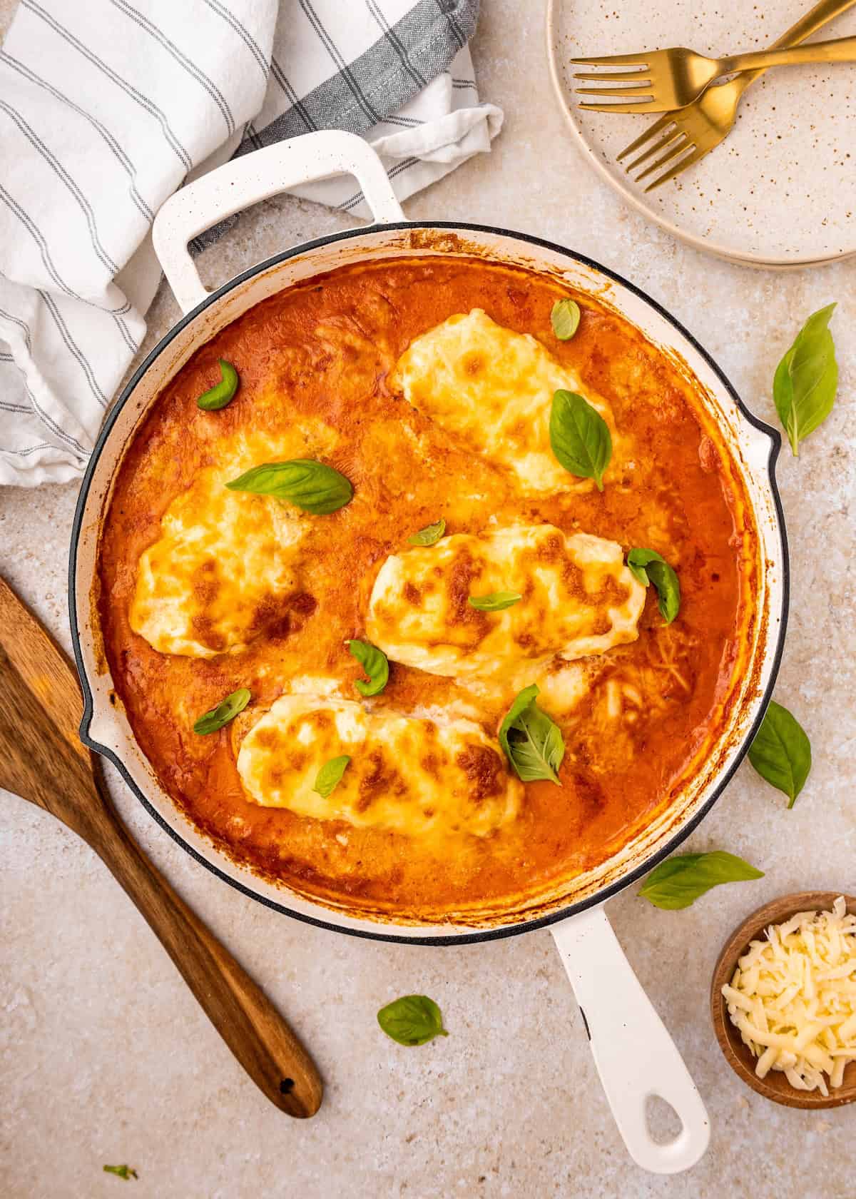 A skillet of cheesy chicken al forno in tomato sauce, garnished with fresh basil leaves.