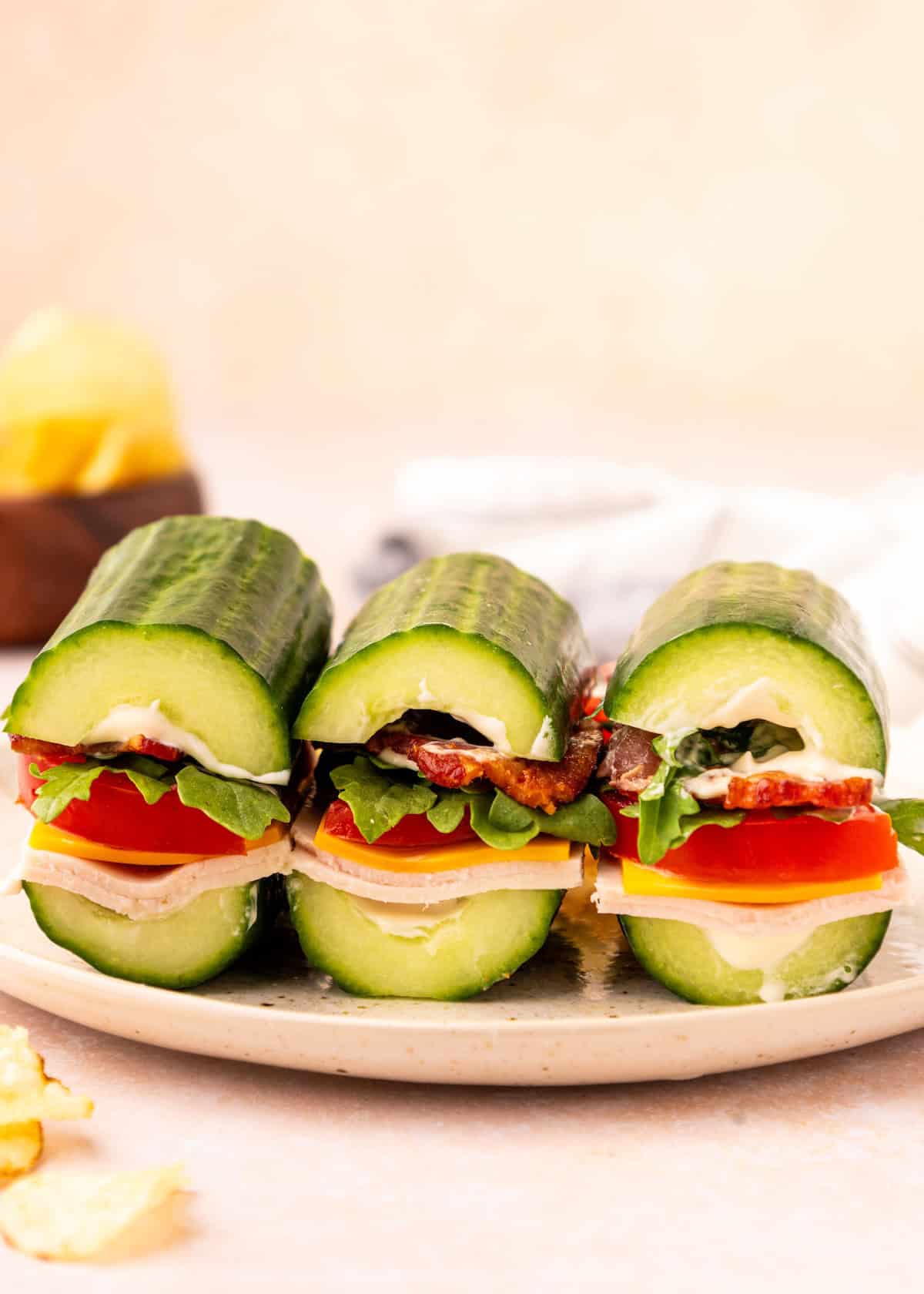 Three cucumber subs filled with lettuce, tomato, bacon, and cheese on a white plate.