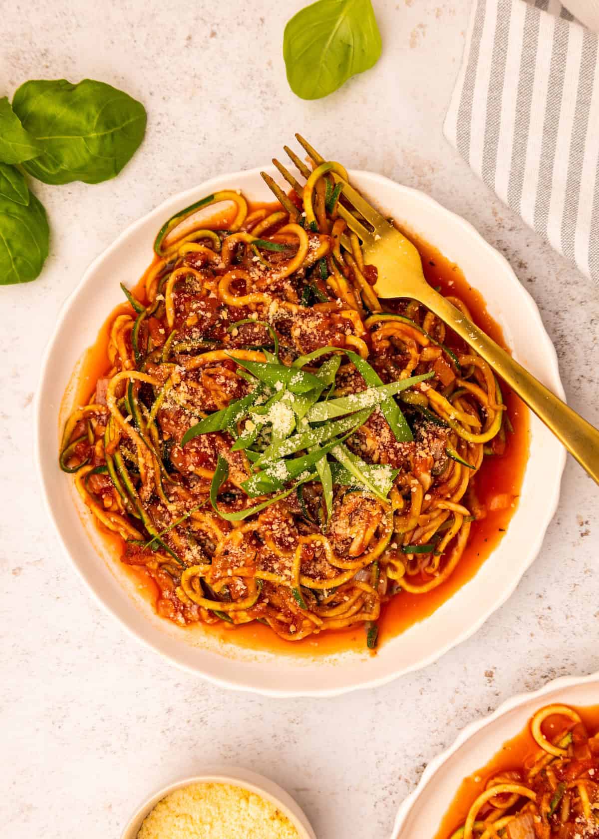 Zucchini Noodle Spaghetti with tomato sauce, basil, and parmesan, served on a white plate.