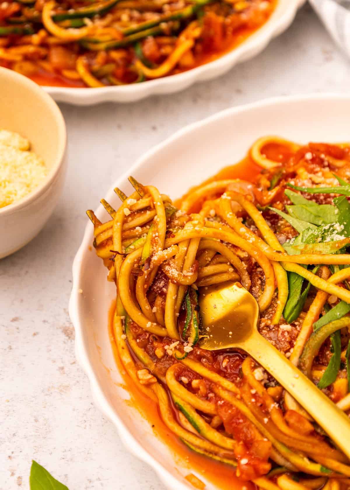 A plate of Zucchini Noodle Spaghetti with tomato sauce, parmesan, and a gold fork.