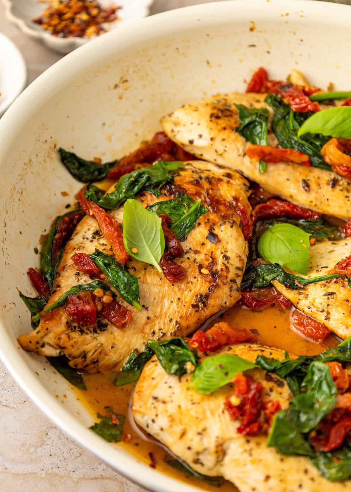 Sun-dried tomato chicken with spinach and basil in a white skillet.