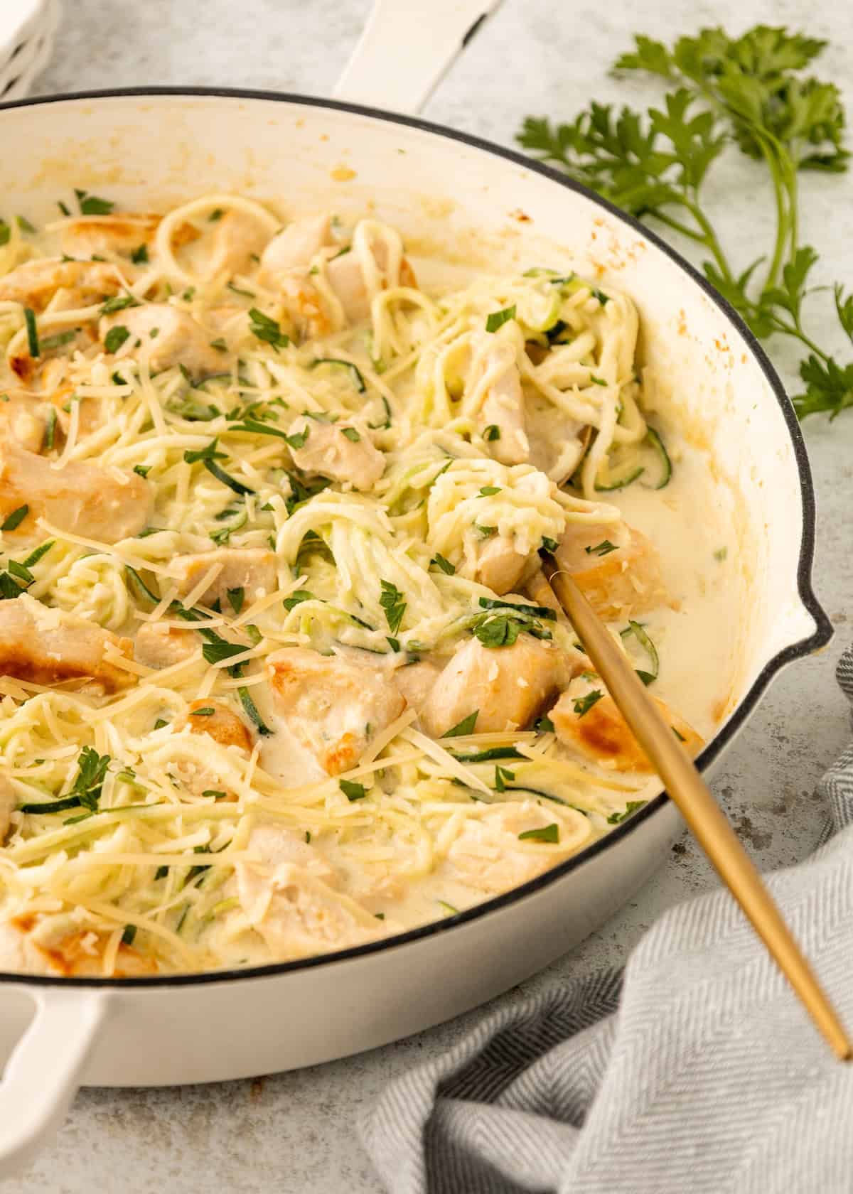 Creamy Chicken Zucchini Noodles with herbs in a white skillet, garnished with parsley.
