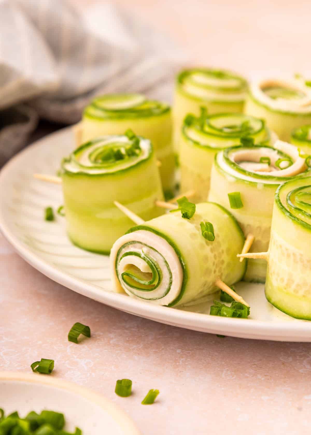 Cucumber rolls with cream cheese on a plate, garnished with fresh chopped chives.