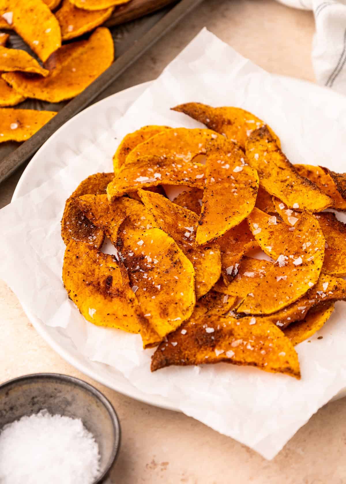 A plate of crispy, seasoned, homemade butternut squash chips sprinkled with salt.