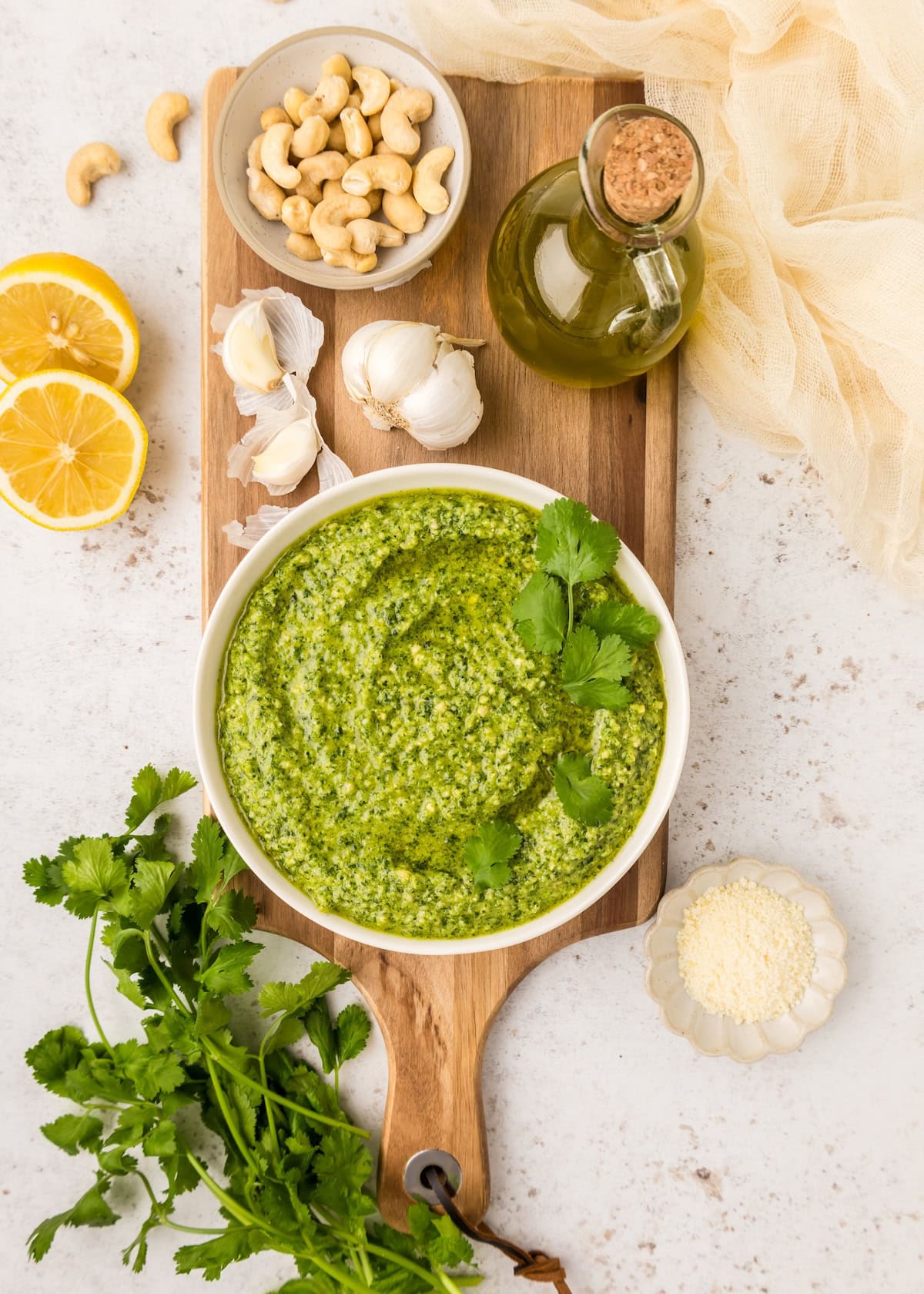 Bowl of cilantro pesto with cashews, garlic, oil, lemon, and cheese on a board.