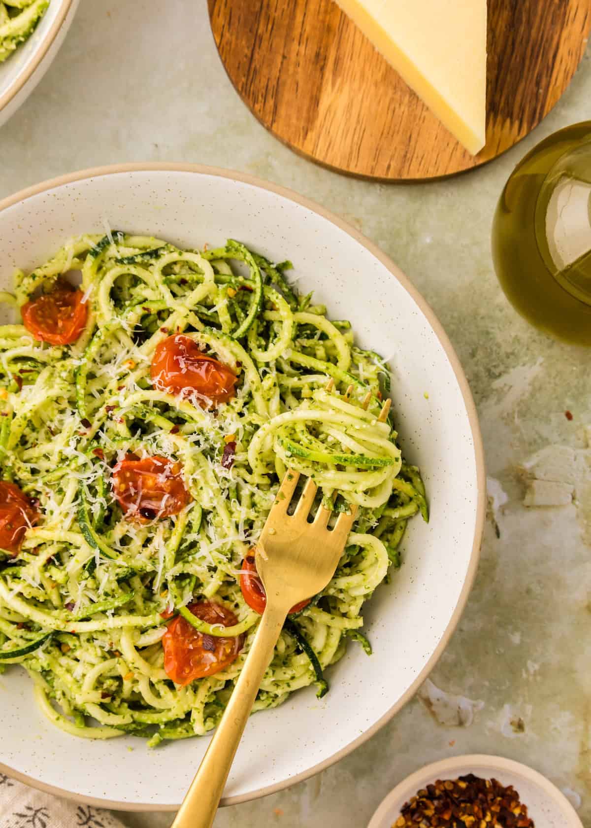 Pesto zucchini noodles topped with roasted tomatoes and cheese, served with a gold fork.