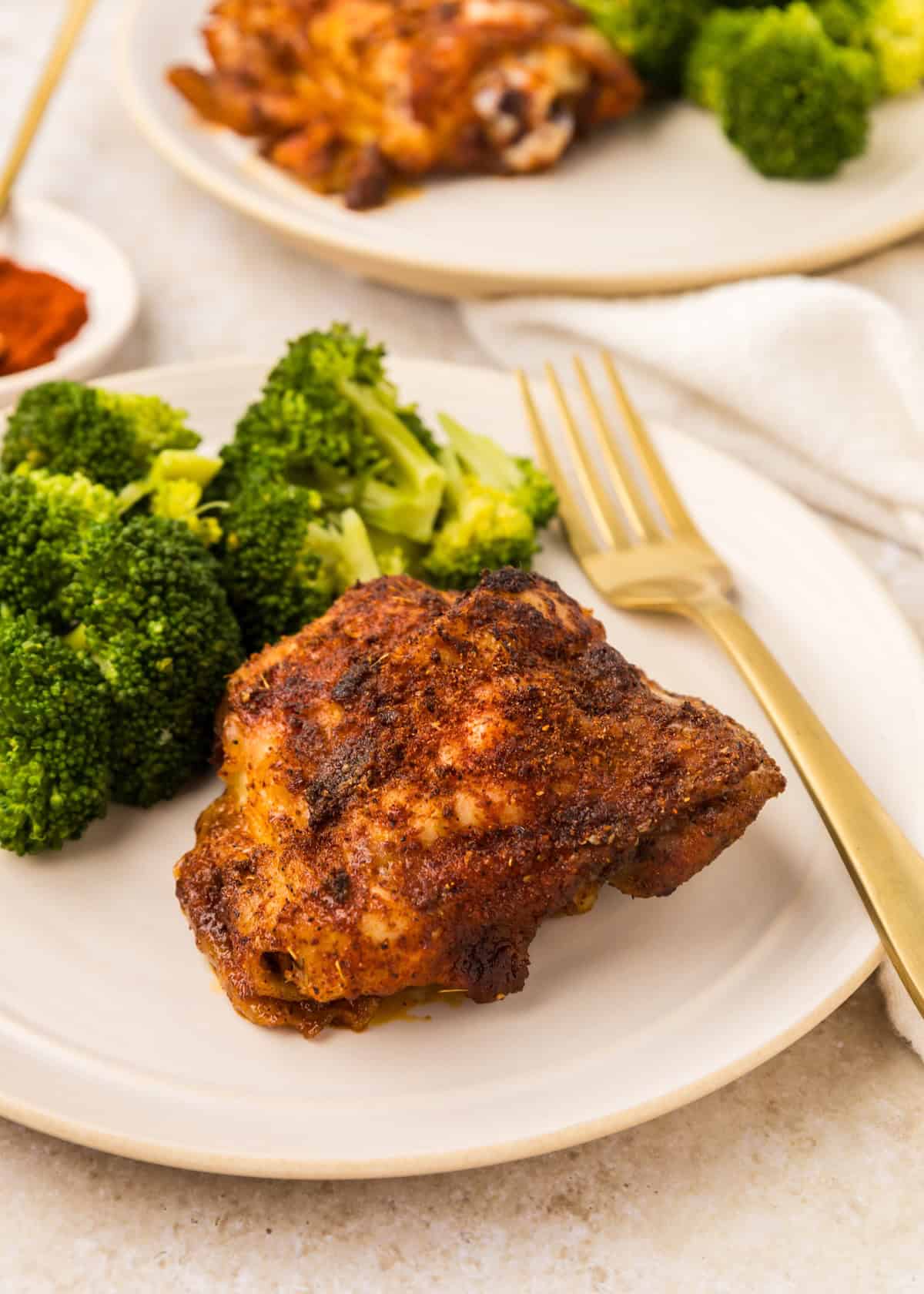 Paprika chicken thigh with steamed broccoli served on a plate with a gold fork.