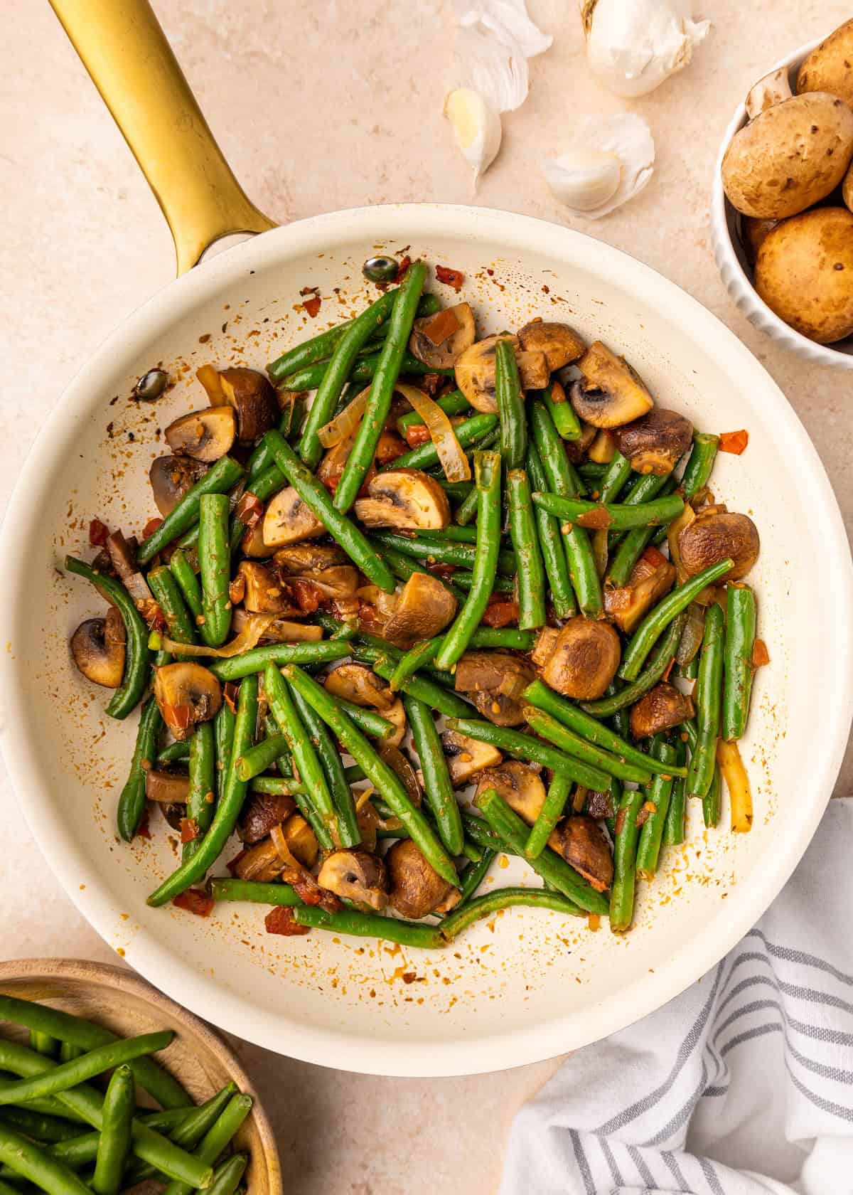Sautéed green beans and mushrooms in a white skillet with a gold handle, perfectly cooked.