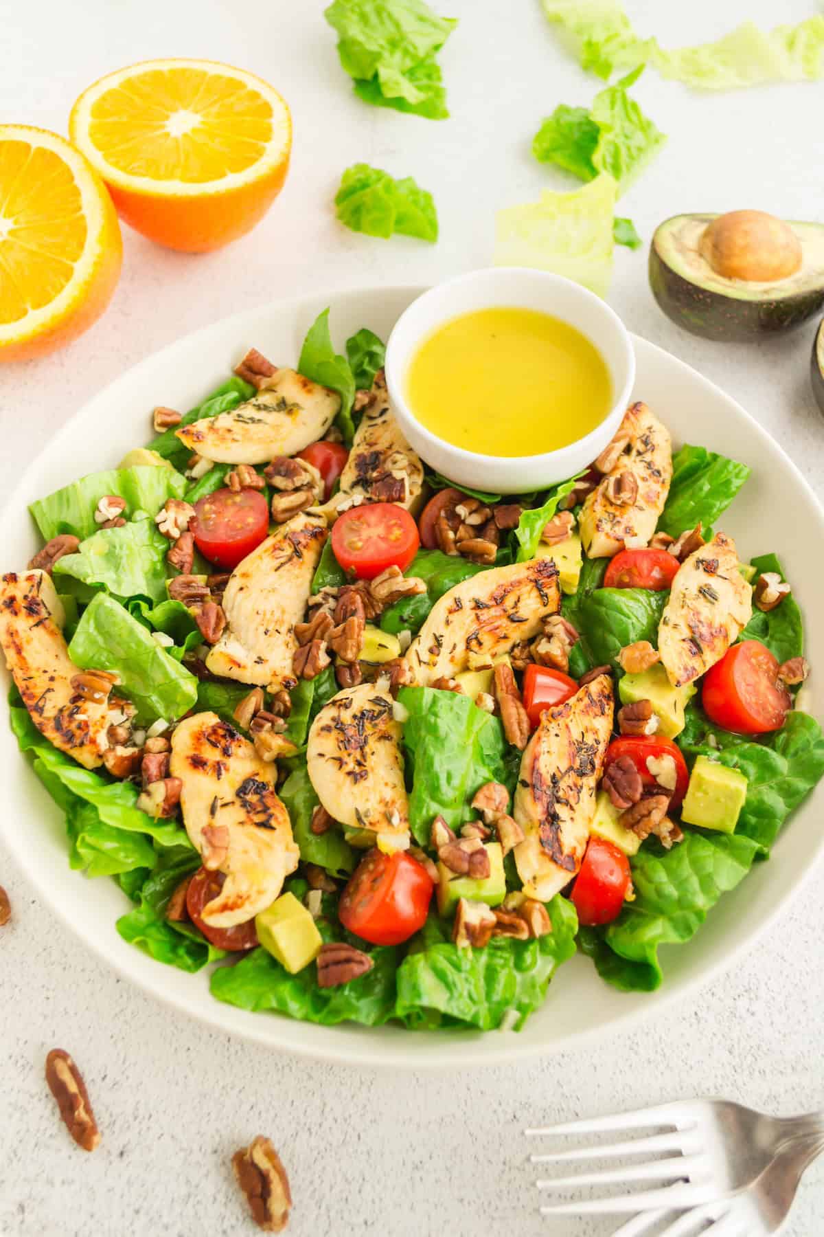 Grilled orange chicken salad with cherry tomatoes, pecans, avocado, and dressing on the side.