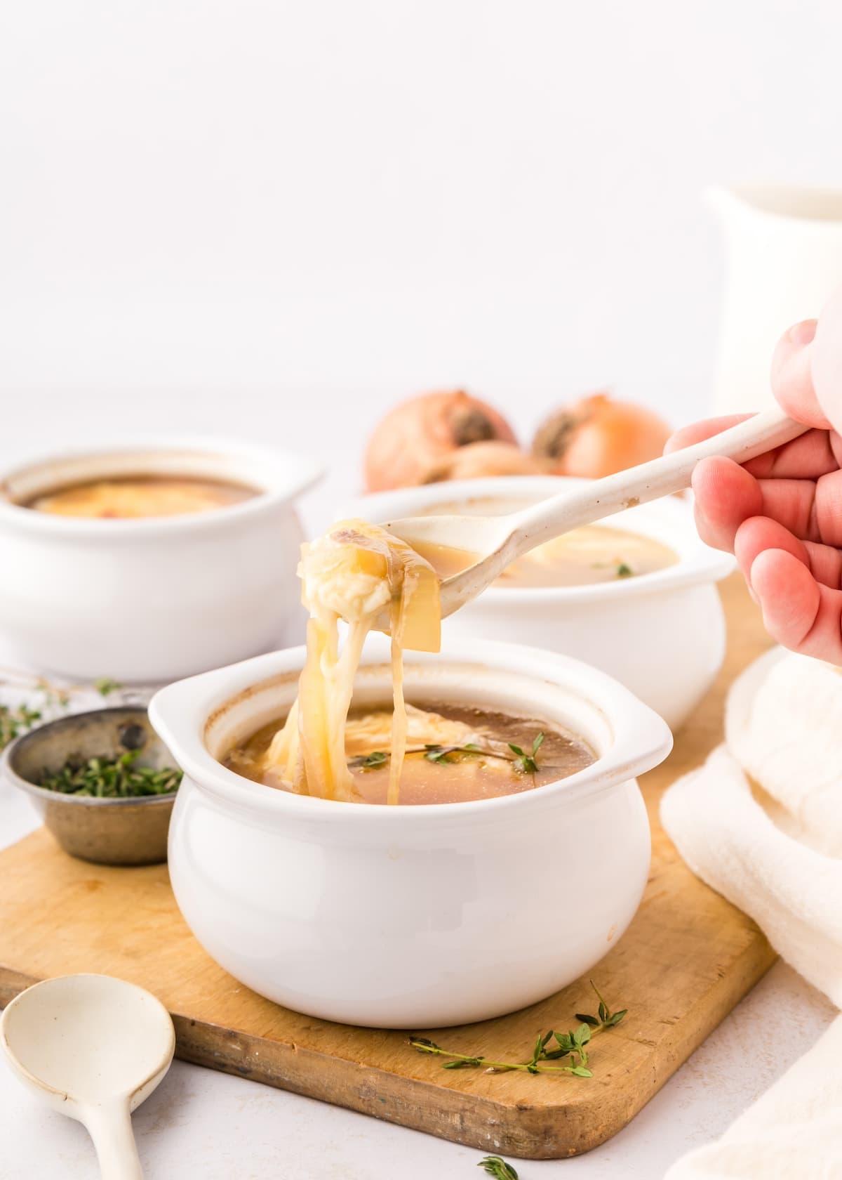 French onion soup in white bowl with stretchy melty cheese.