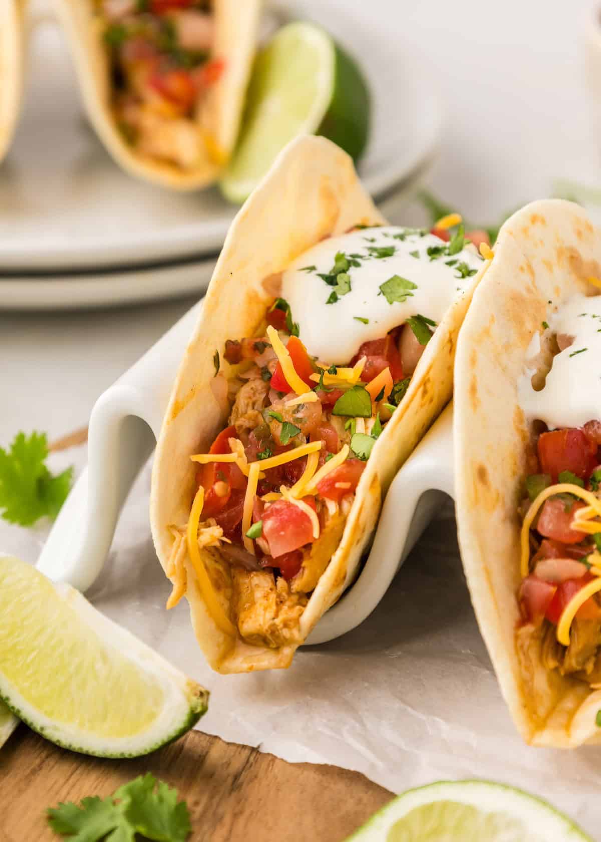 Crockpot shredded chicken tacos with cheese, salsa, sour cream, cilantro, and lime wedges.
