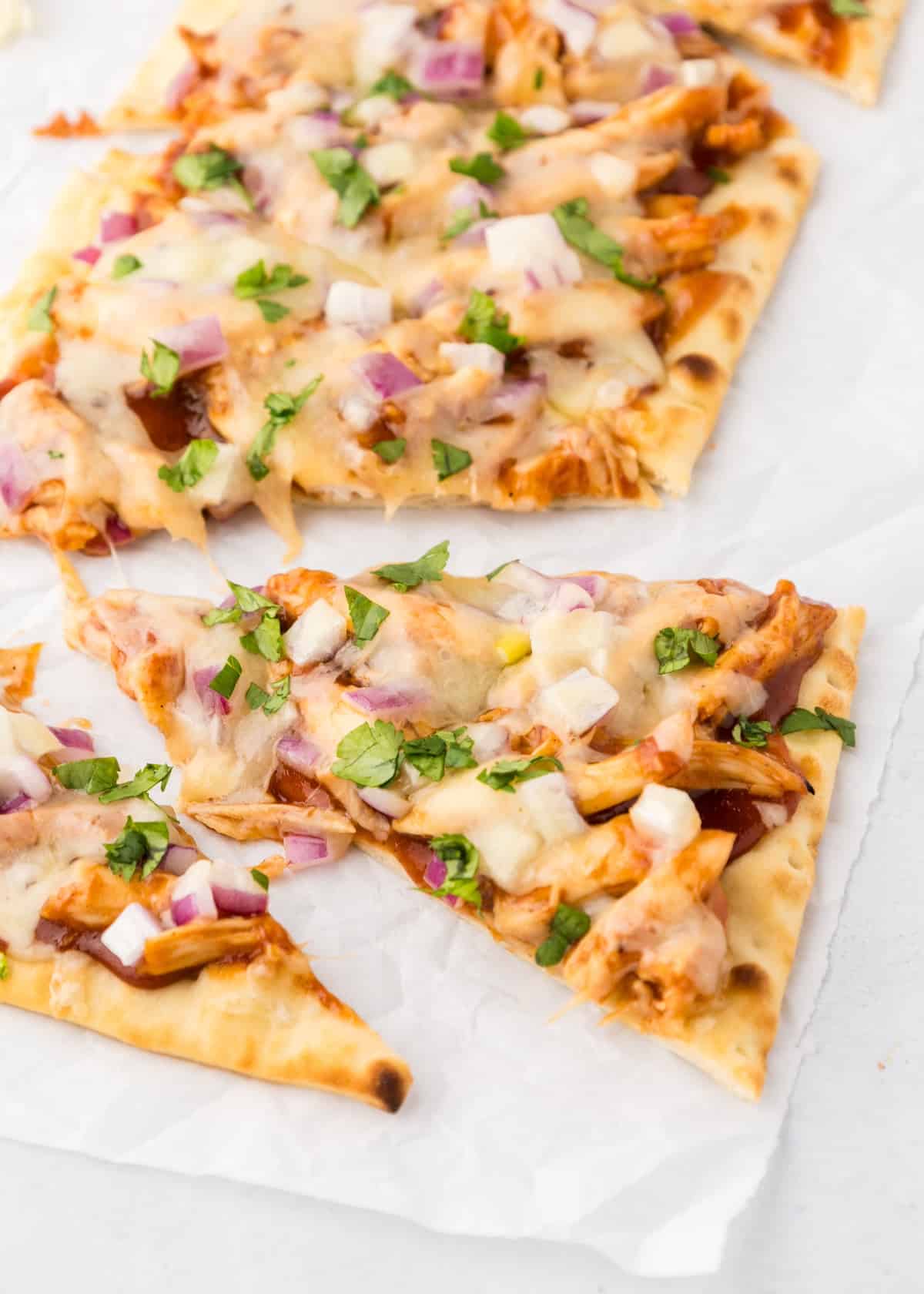 BBQ chicken flatbread sliced and on parchment paper.