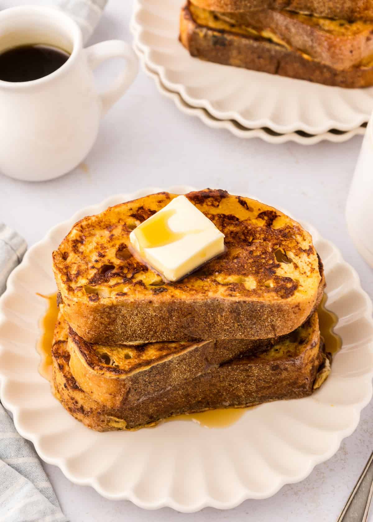 Stack of Sourdough French Toast with syrup and butter, coffee in the background.