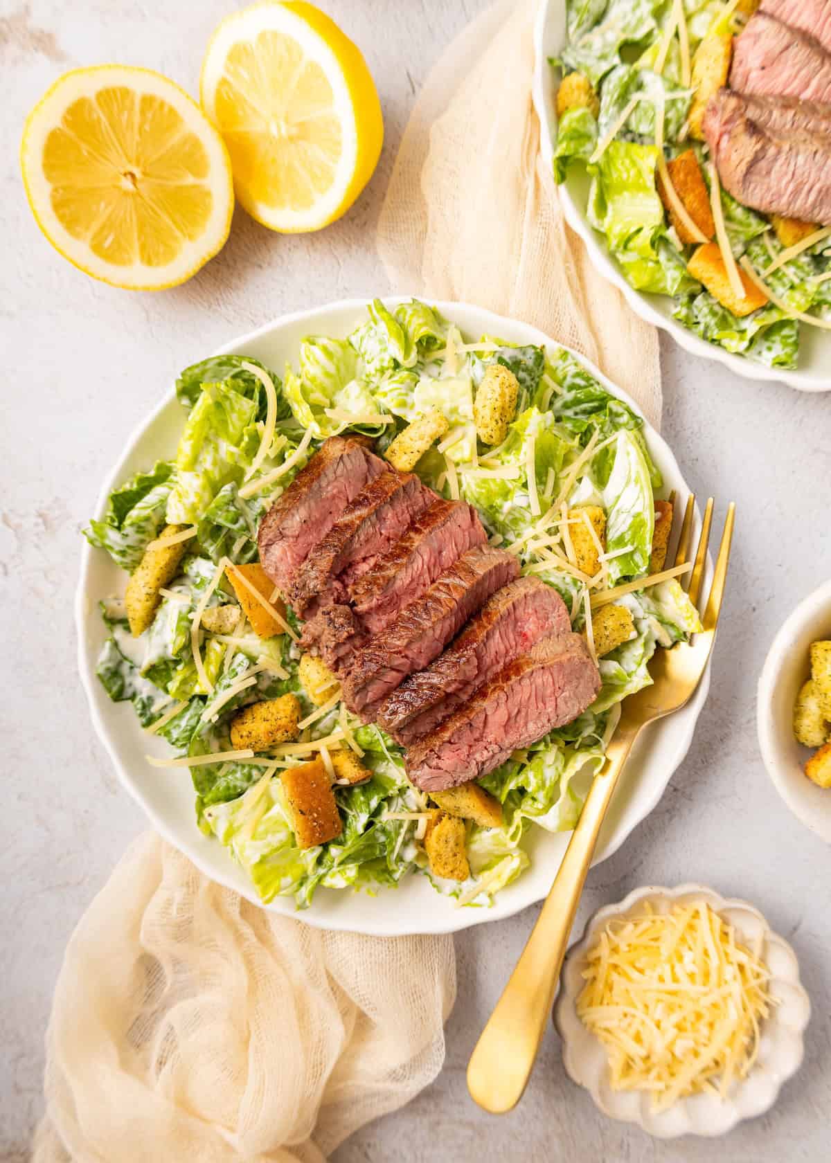 Steak Caesar Salad topped with croutons and parmesan, served with fresh lemon halves.