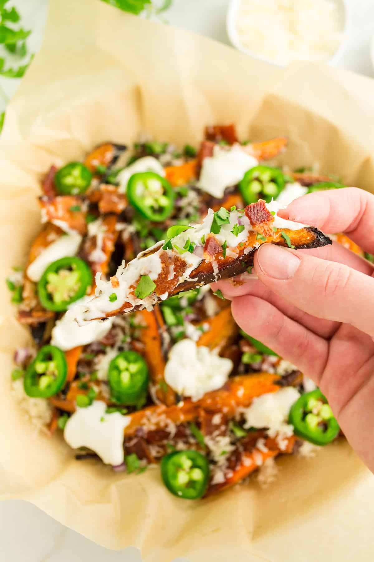 A hand holds loaded sweet potato fries topped with jalapeno, cilantro, and sour cream.