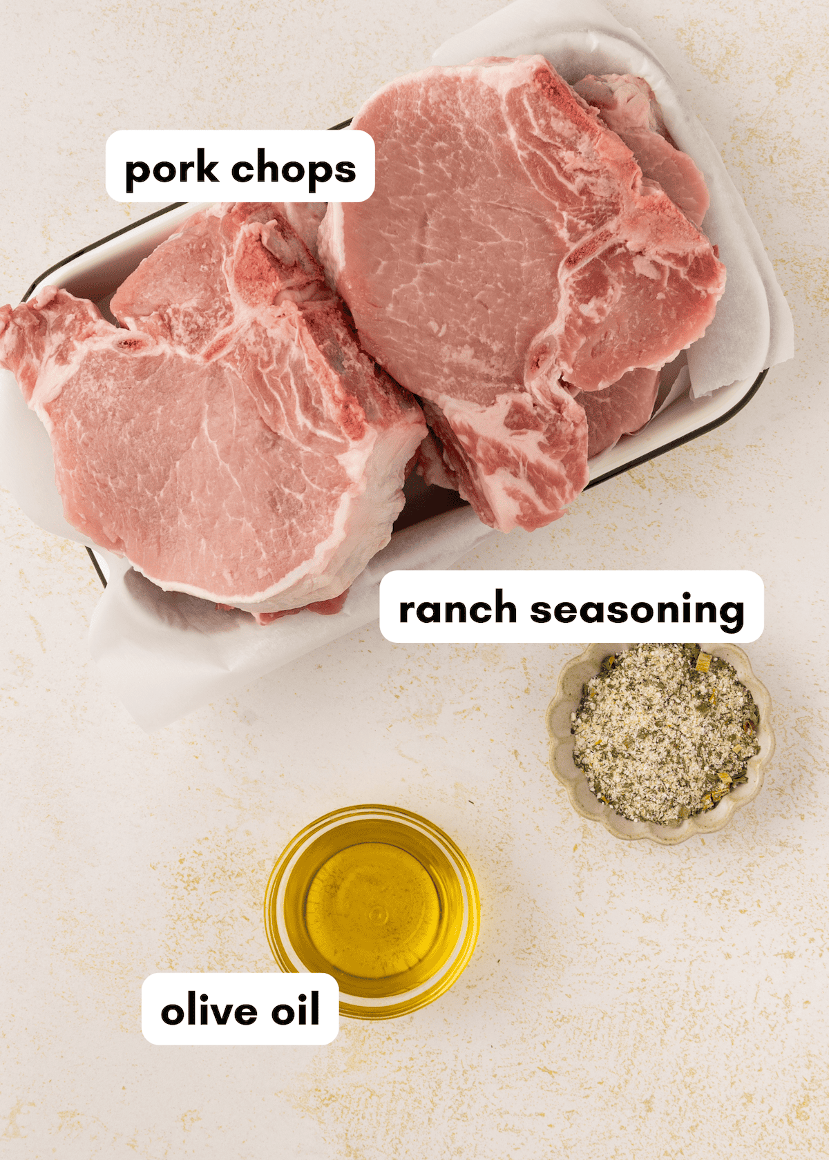 Baked Ranch Pork Chops in a tray with ranch seasoning and olive oil on a light surface.