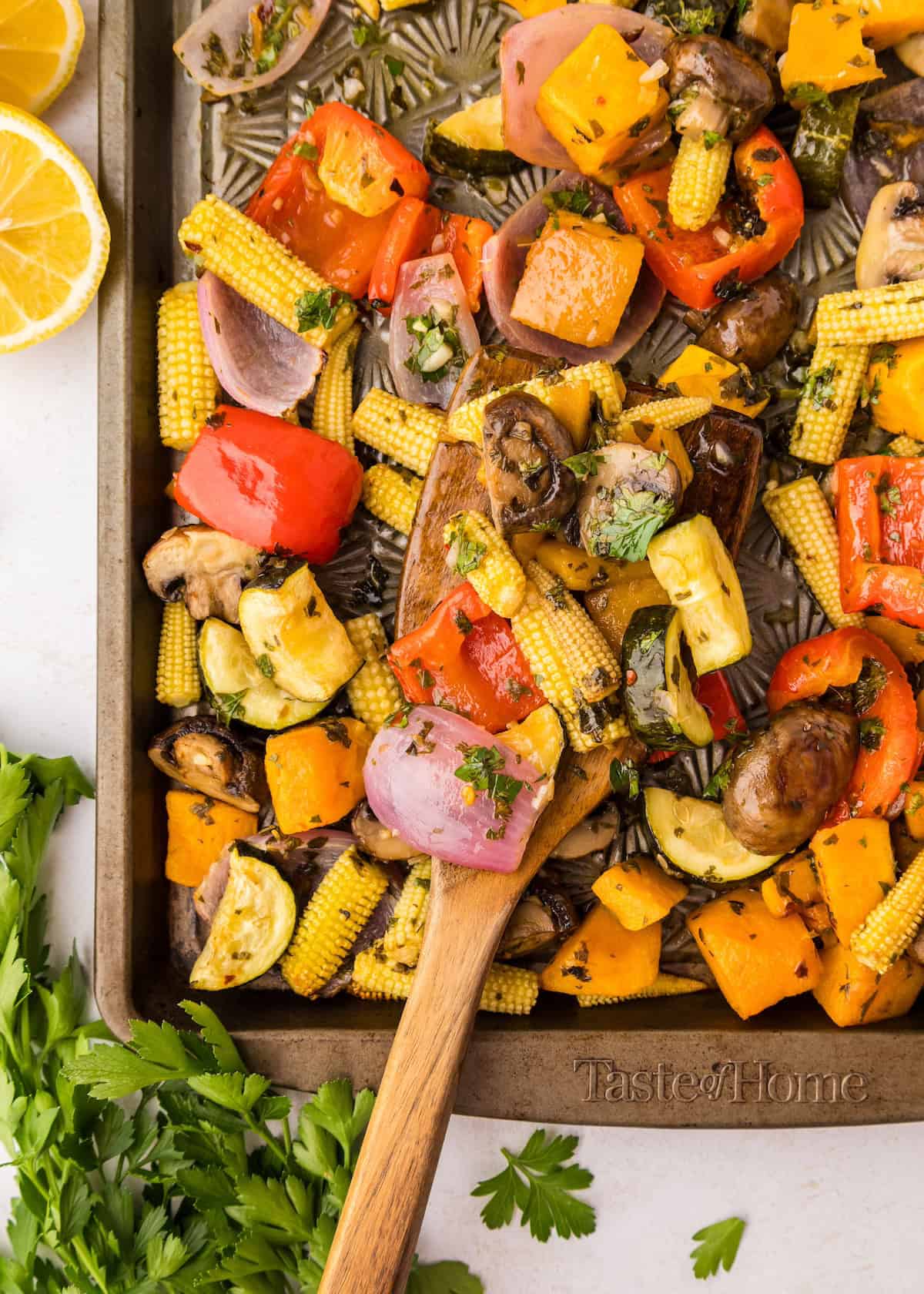 Chimichurri roasted vegetables, including corn and peppers, on a baking tray with a spoon.