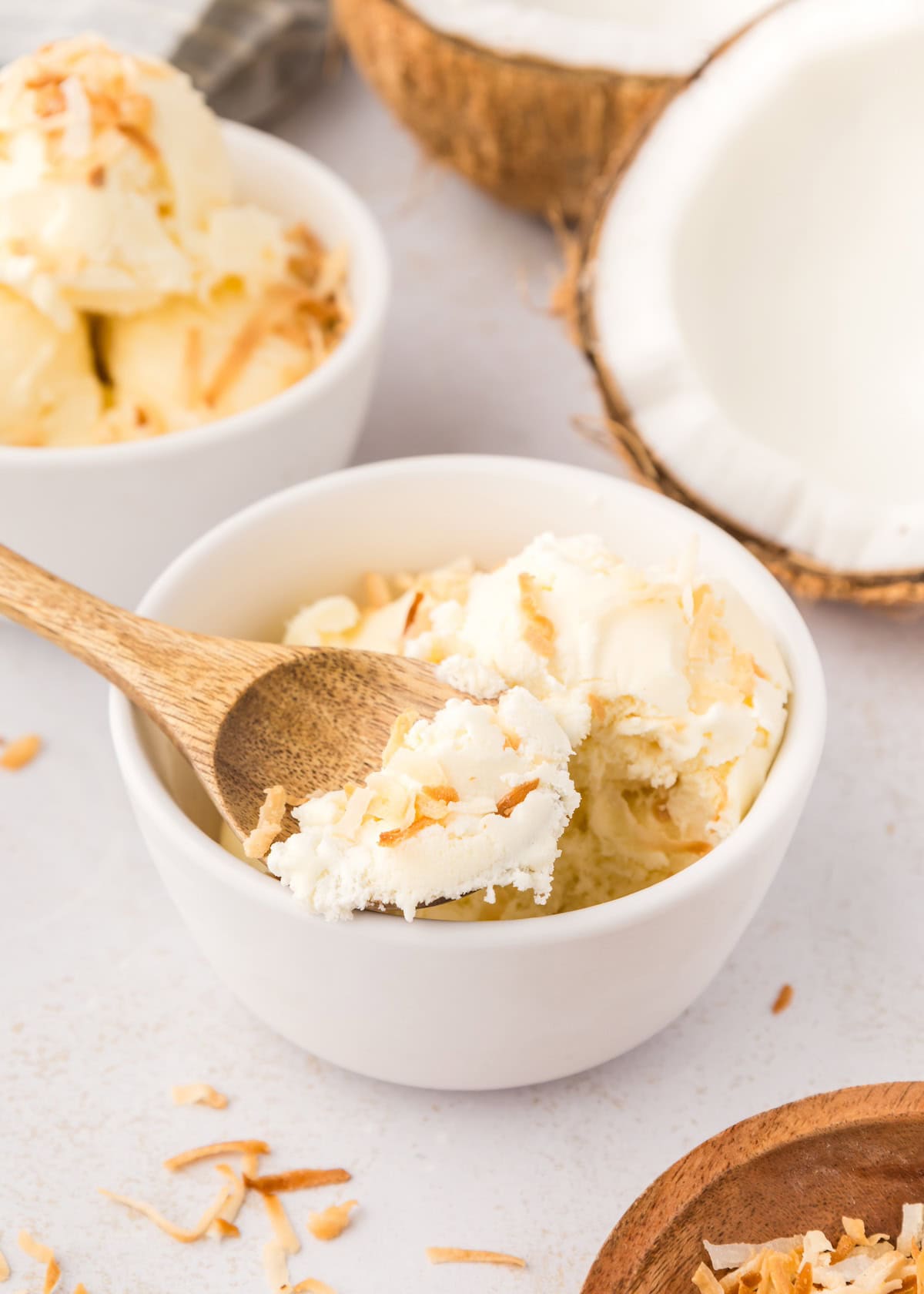 Bowl of no churn coconut ice cream with toasted coconut flakes and a wooden spoon.