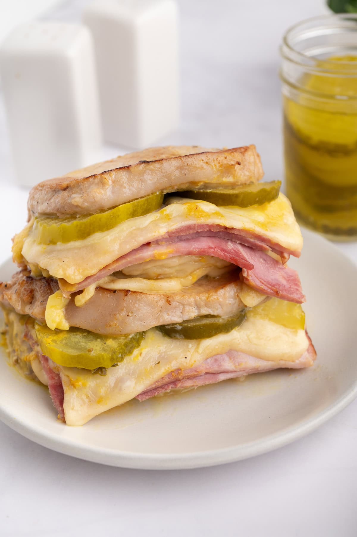 Stacked Cuban sandwich halves with ham, cheese, cuban pork, and pickles on a white plate.