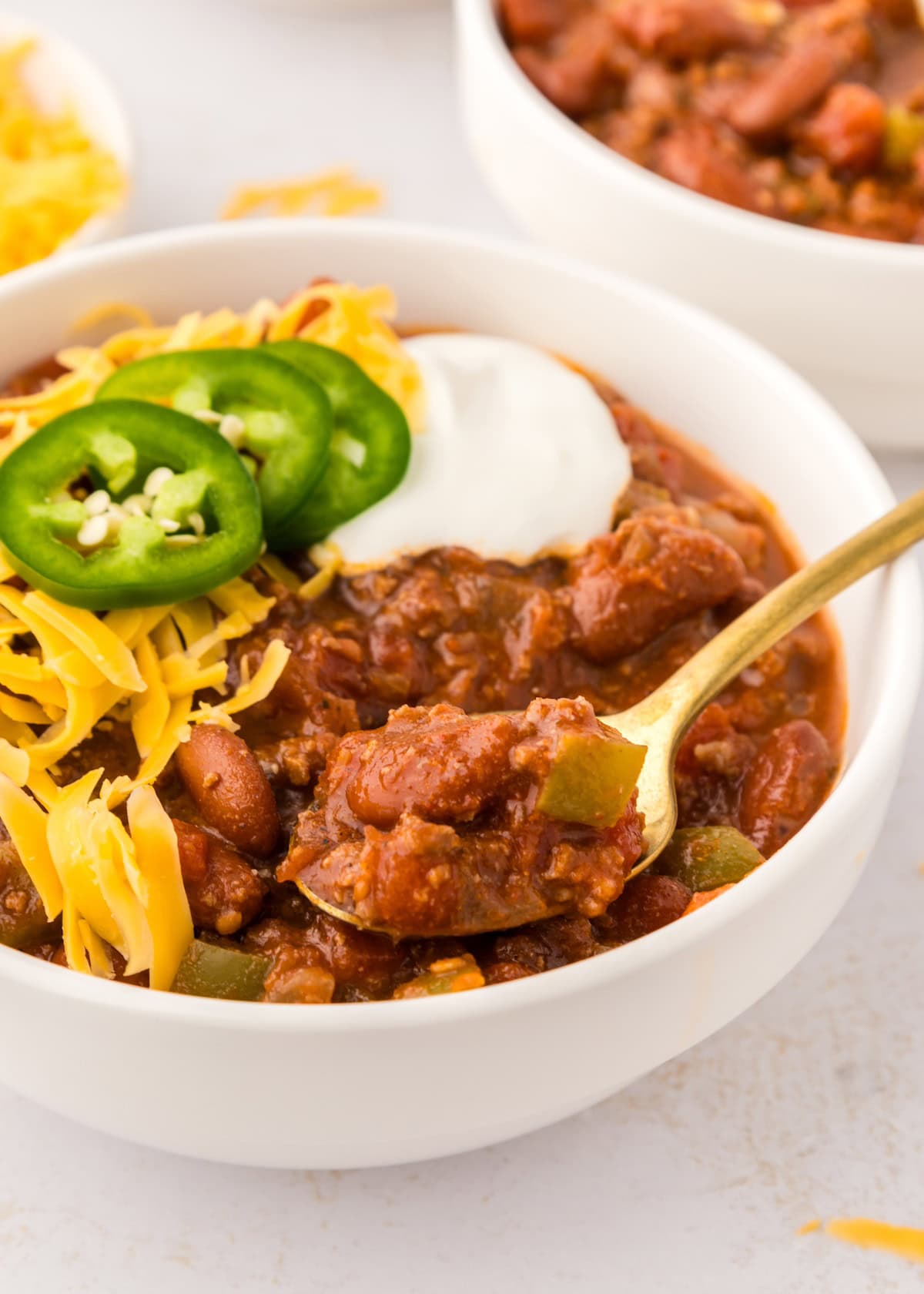 Bowl of Instant Pot Chili topped with shredded cheese, jalapeño slices, and sour cream.