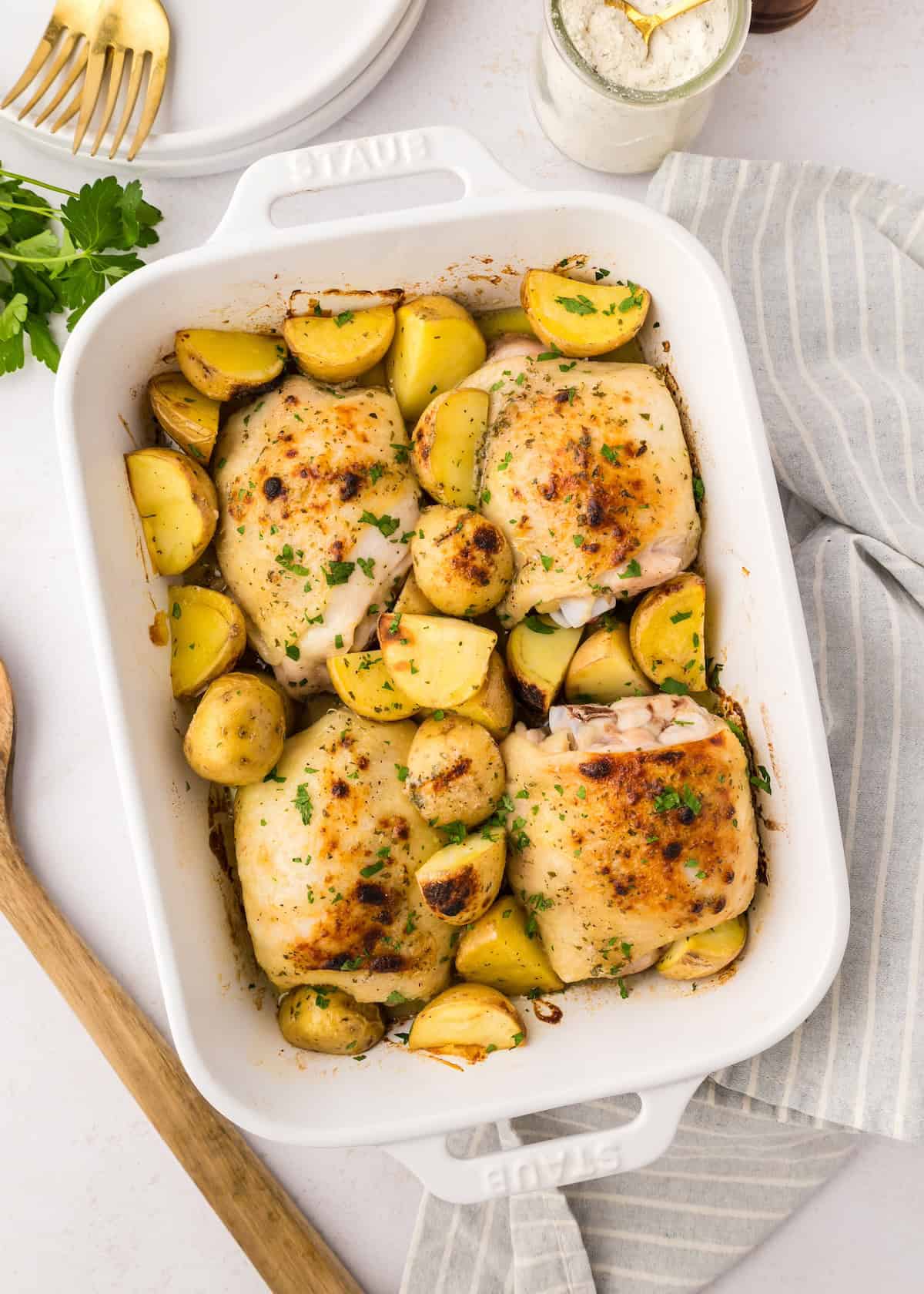 Baked Ranch Chicken Thighs and potatoes in a white dish, garnished with fresh herbs.