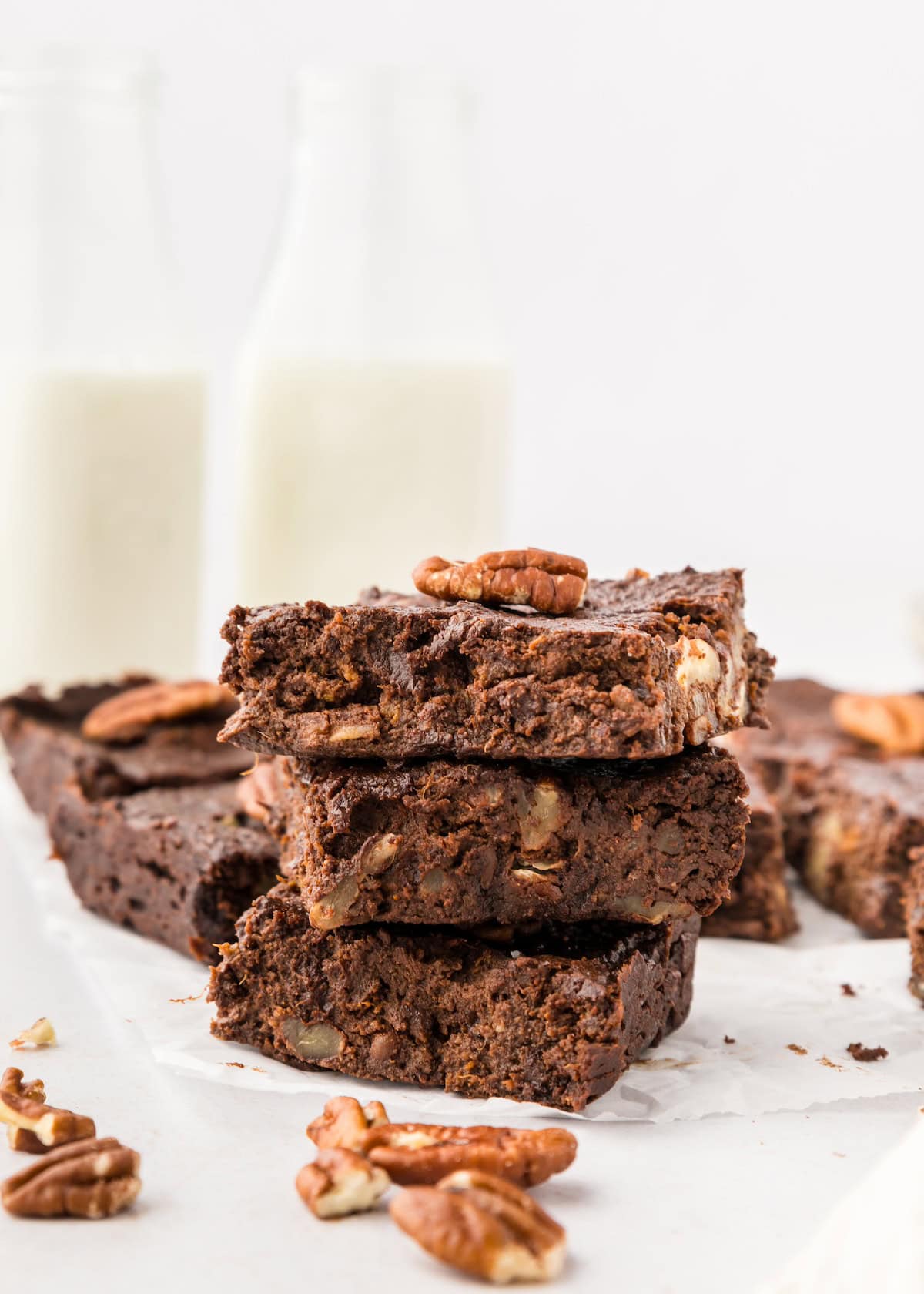 Three sweet potato brownies stacked with pecans, and two bottles of milk in the background.
