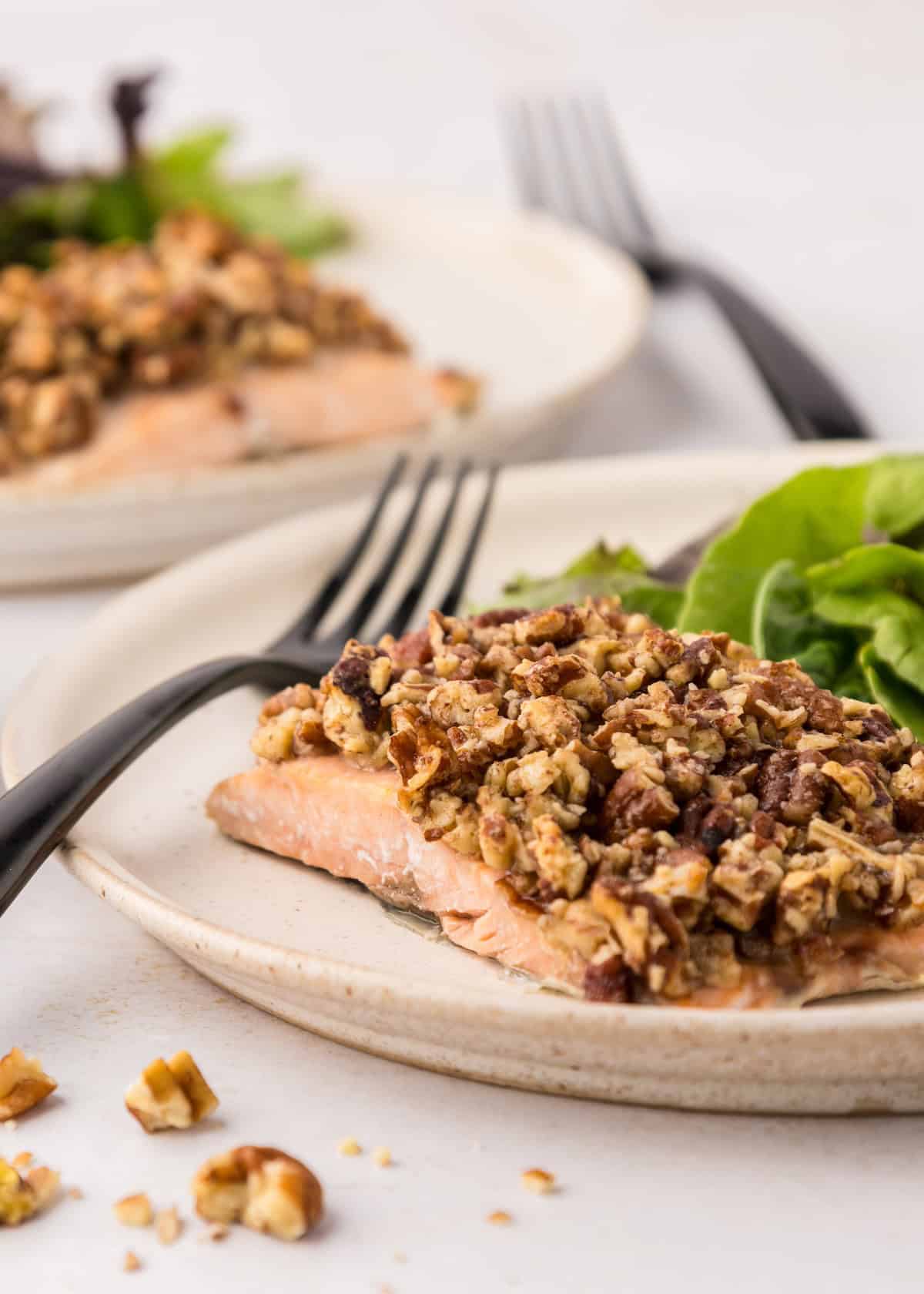 Pecan Crusted Salmon fillet topped with nuts, served with greens and a black fork.