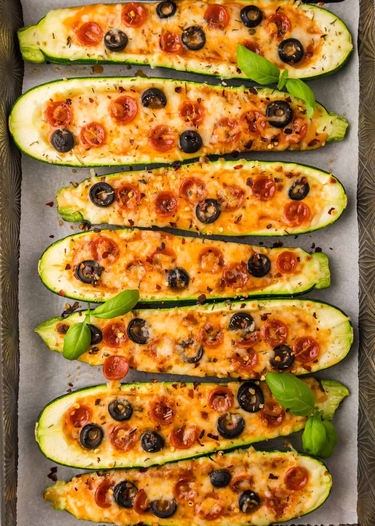 Six zucchini pizza boats topped with melted cheese, pepperoni, black olives, and fresh basil.