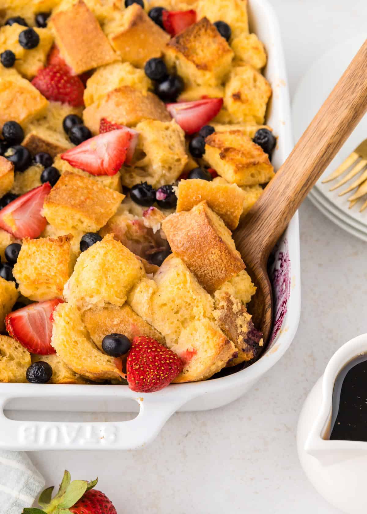 Berry French Toast Casserole with strawberries, blueberries, and a wooden serving spoon.