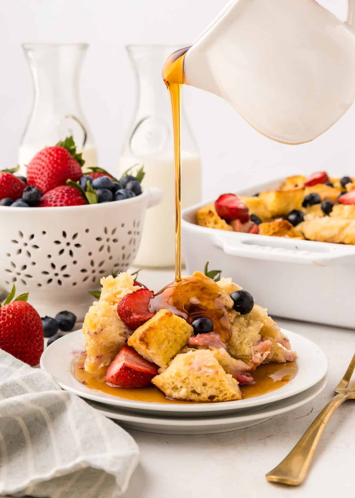 Syrup poured over Berry French Toast Casserole topped with strawberries and blueberries.
