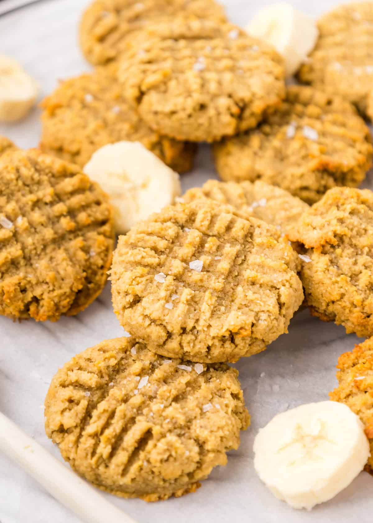 Peanut Butter Banana Cookies with fork marks, sprinkled with salt, beside banana slices.