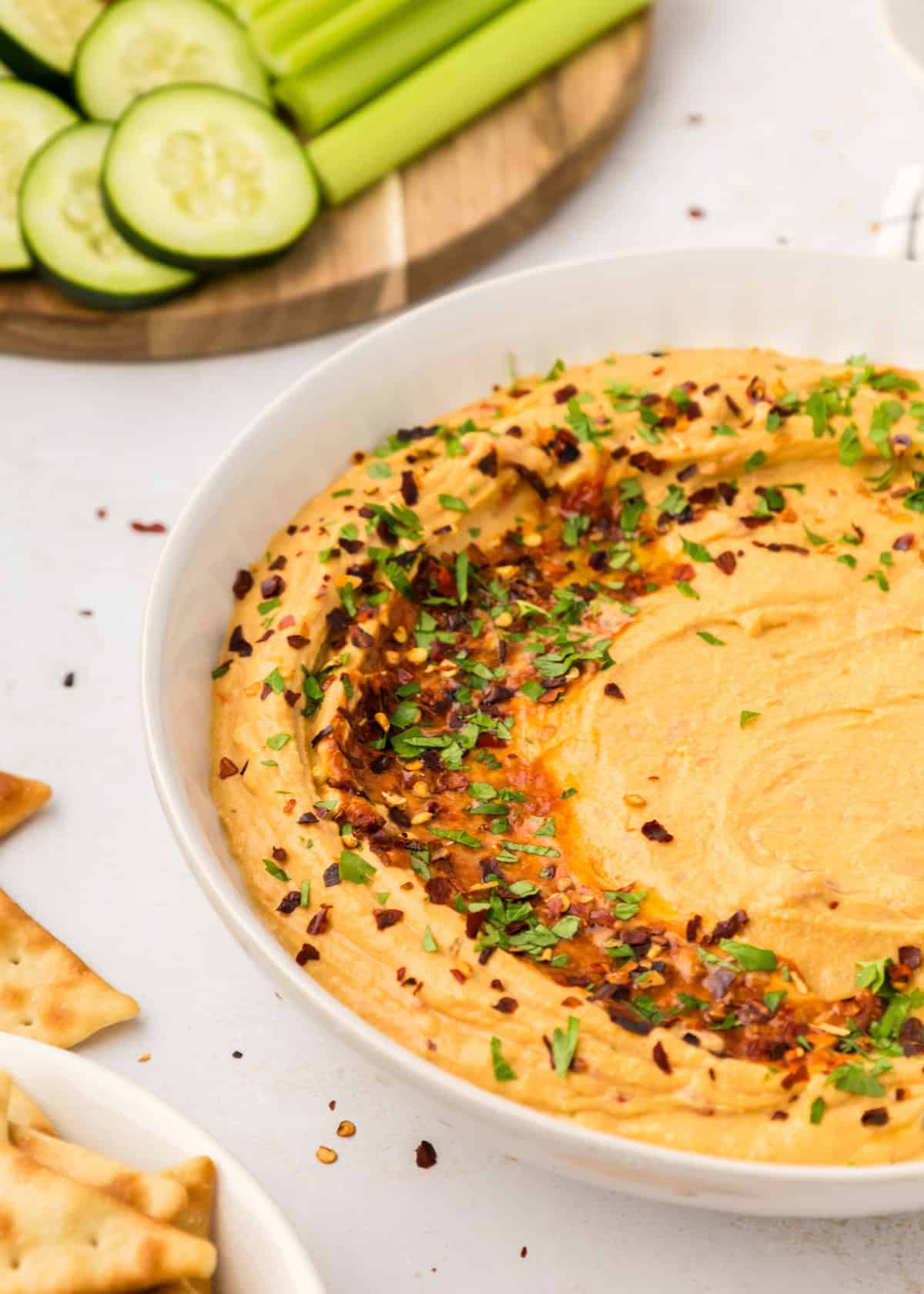 A bowl of Roasted Red Pepper Hummus topped with herbs, served with veggies and crackers.