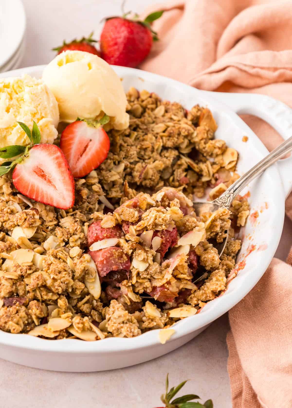 A dish of Strawberry Rhubarb Crisp with ice cream and fresh strawberries on top.