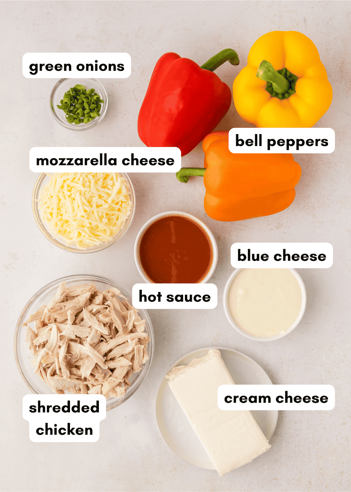 Assorted labeled ingredients for Buffalo Chicken Stuffed Peppers on a light background.