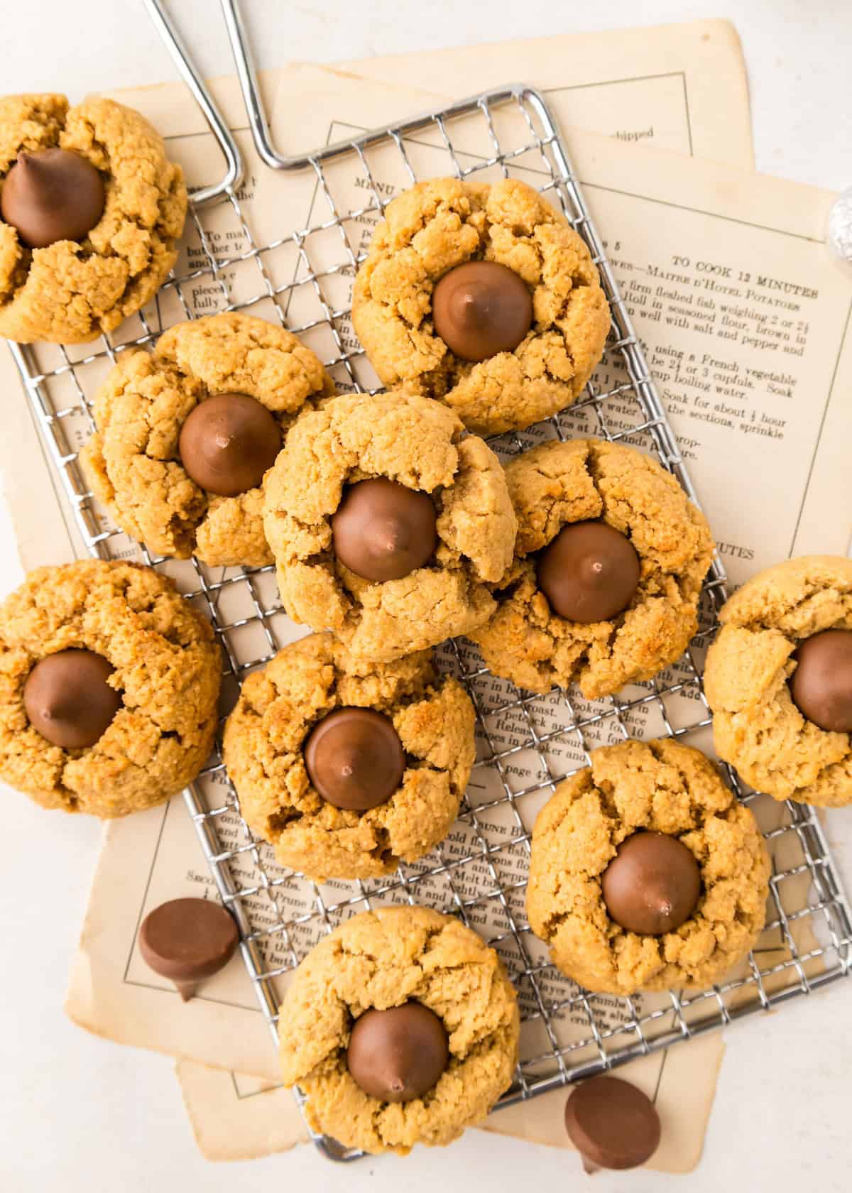 Gluten-Free Peanut Butter Blossoms with chocolate centers on a cooling rack and old recipe pages.