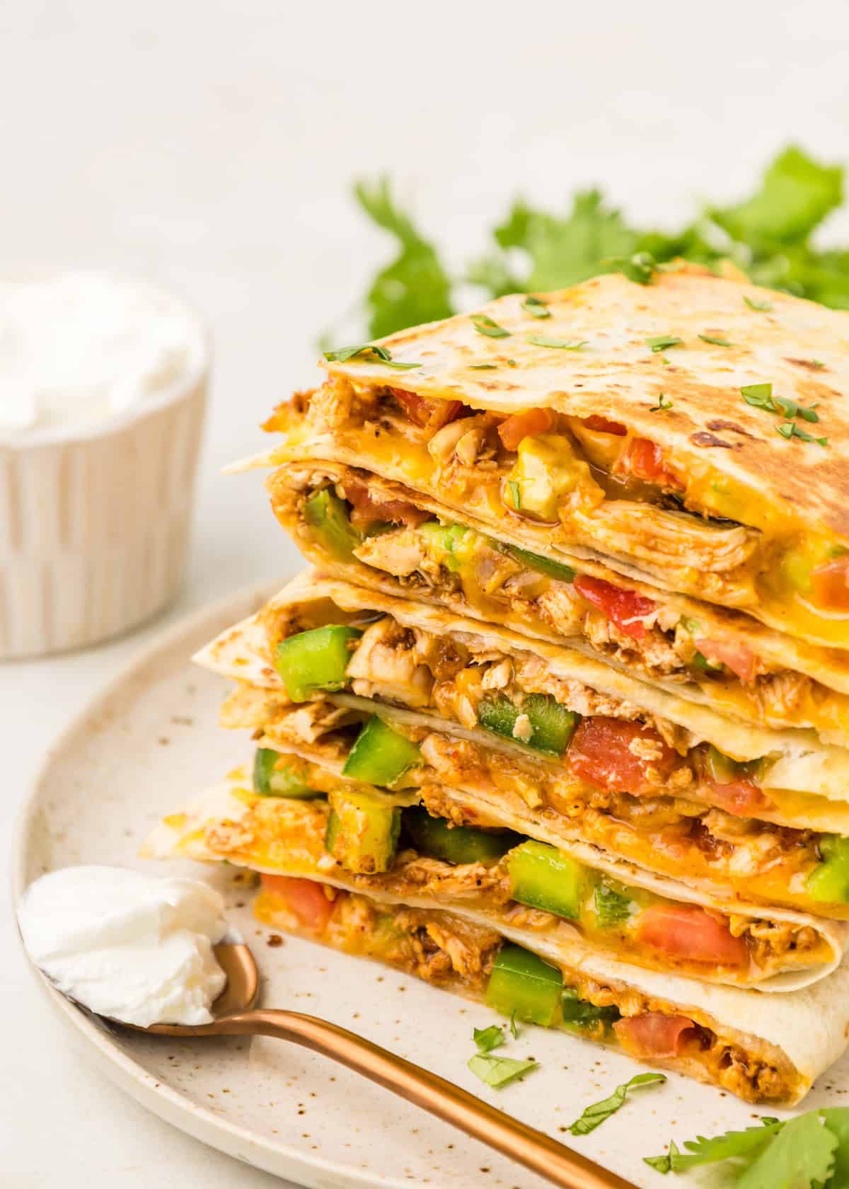 Chicken Quesadillas served with sour cream. Stacked on a plate.