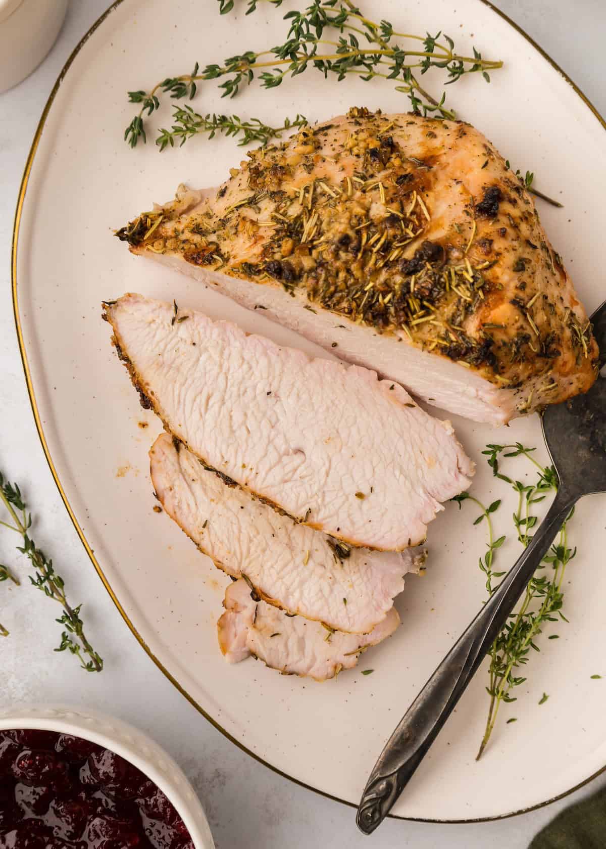 Herb Roasted Turkey Breast, sliced and served with fresh herbs and a serving fork.