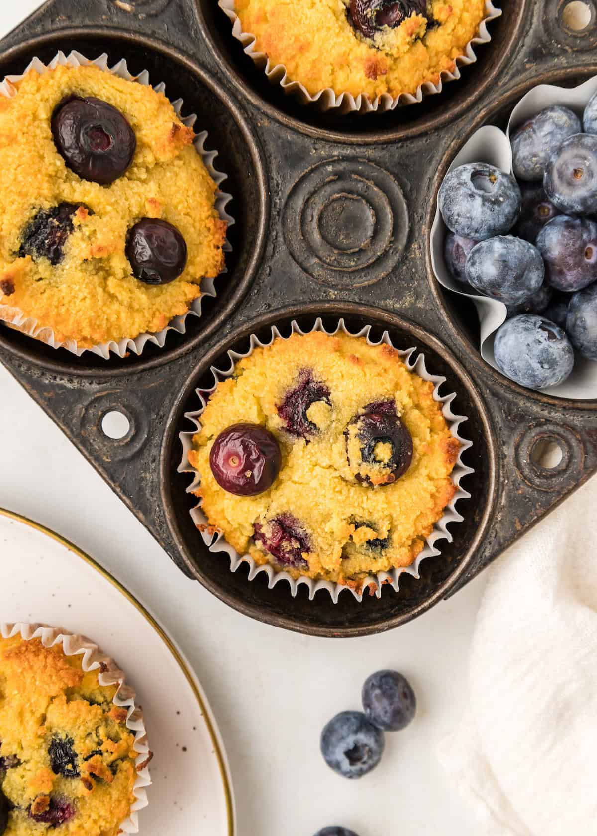 Overhead view of gluten-free blueberry muffins in a tin next to fresh blueberries.