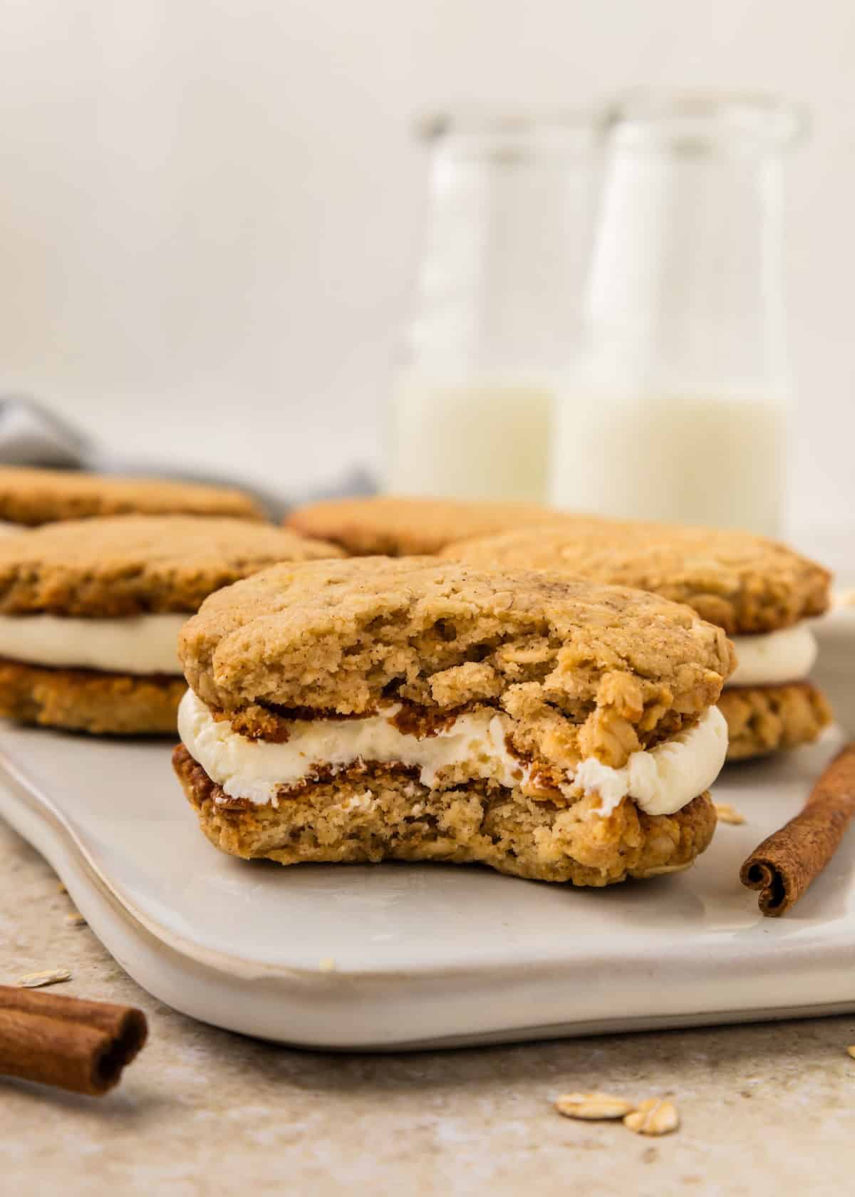 Oatmeal Cream Pies on a platter, one bitten, with bottles of milk in the background.