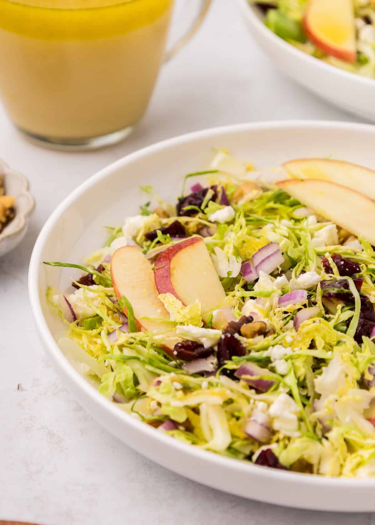 Shaved Brussels Sprouts Salad with apple slices, red onions, walnuts, and cranberries in a bowl.