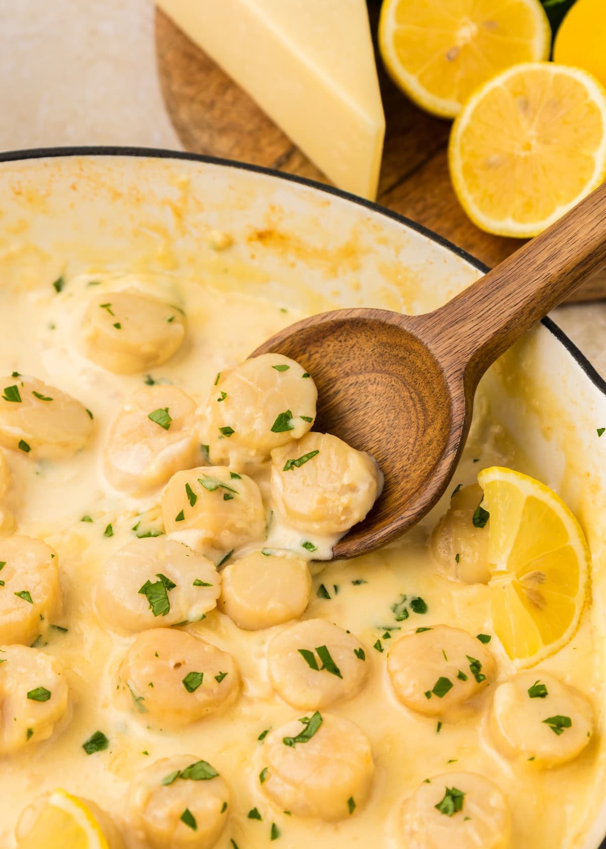 Creamy Garlic Scallops in a skillet with lemon and parsley, stirred with a wooden spoon.