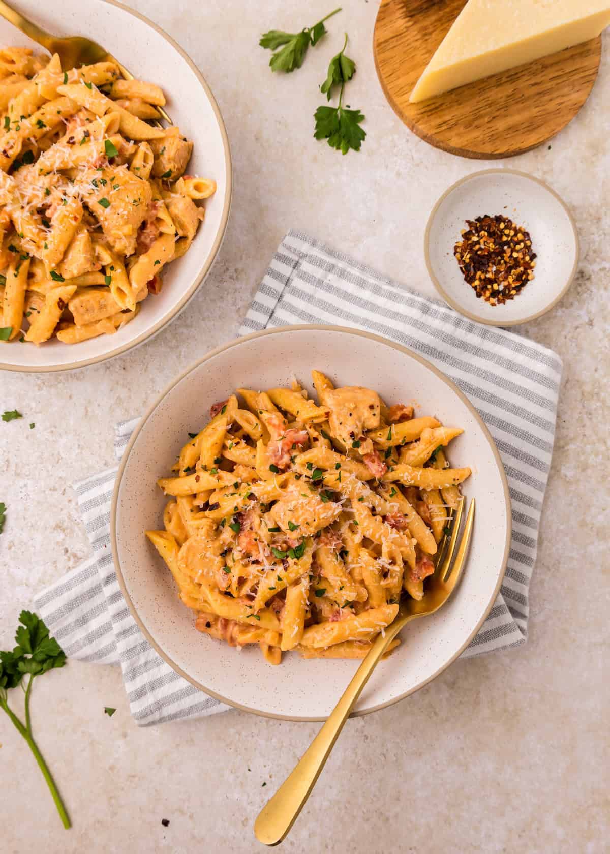 Two bowls of creamy Cajun Chicken Pasta with herbs, cheese, and a gold fork on a striped napkin.