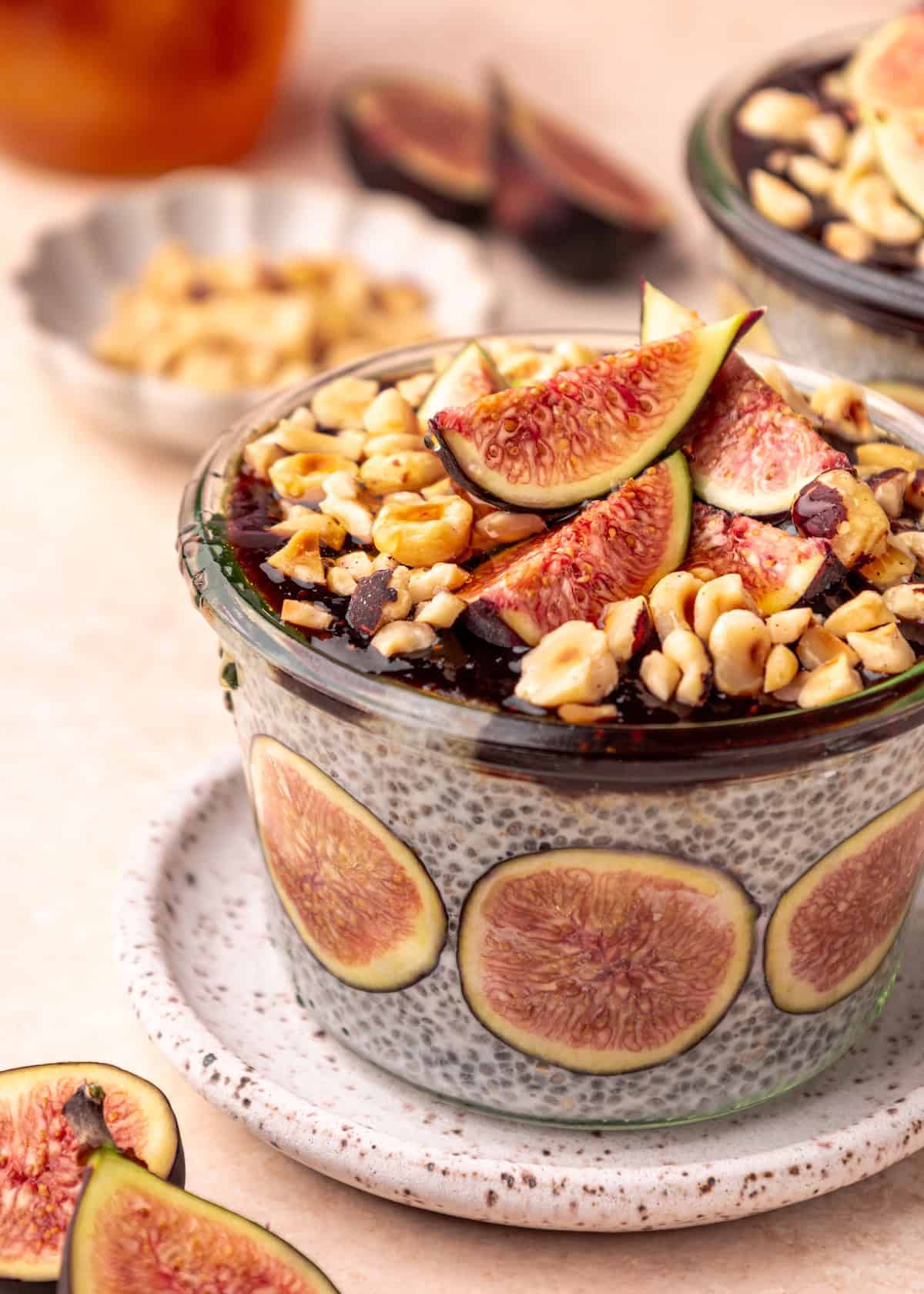 Glass jar of Fig Chia Pudding topped with fresh figs and chopped nuts on a speckled plate.
